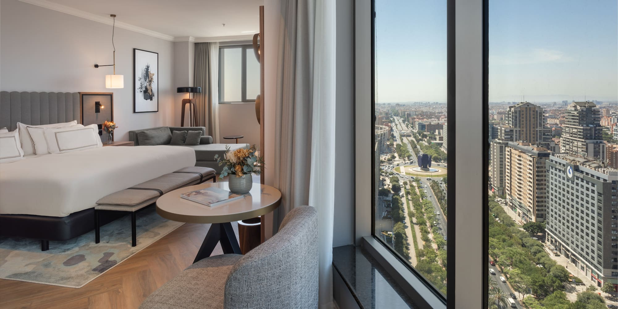 Habitación de hotel moderna con cama, sala y vista panorámica a la ciudad de Madrid.