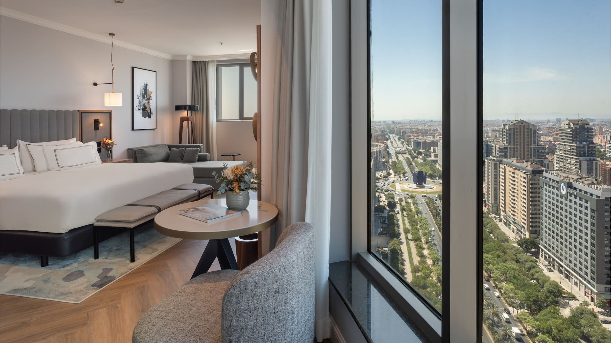 Habitación de hotel moderna con cama, sala y vista panorámica a la ciudad de Madrid.