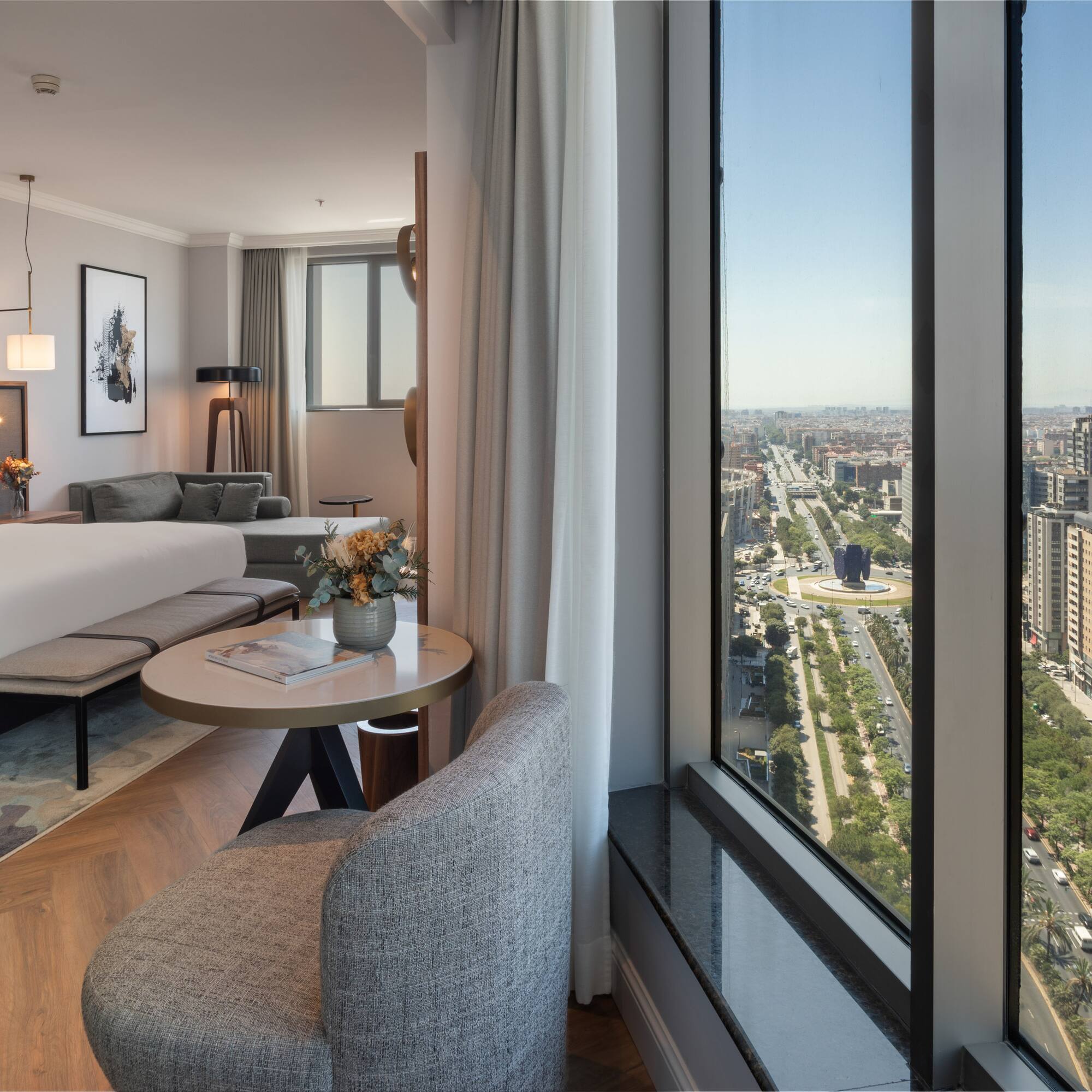 Habitación de hotel moderna con cama, sala y vista panorámica a la ciudad de Madrid.