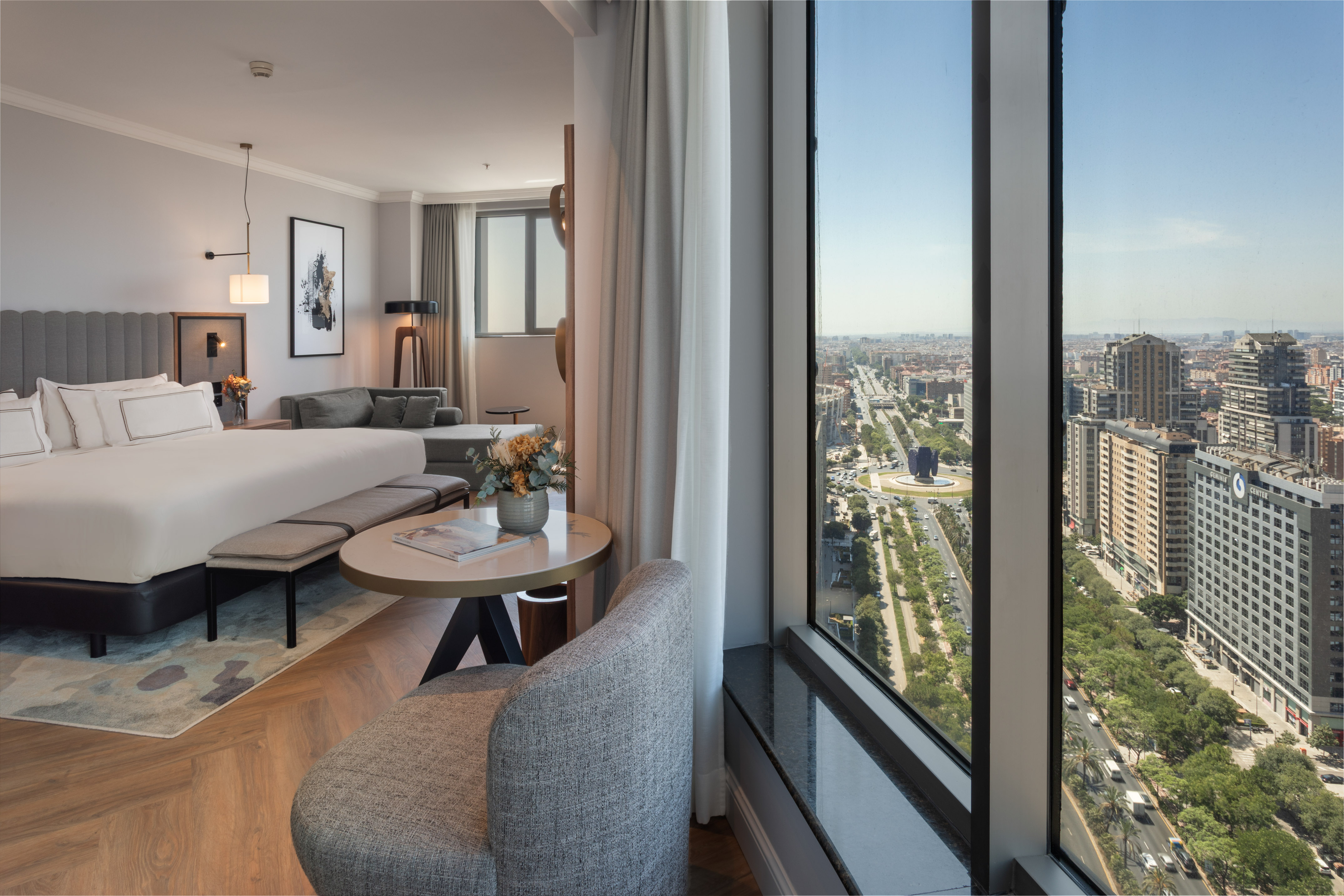 Habitación de hotel moderna con cama, sala y vista panorámica a la ciudad de Madrid.