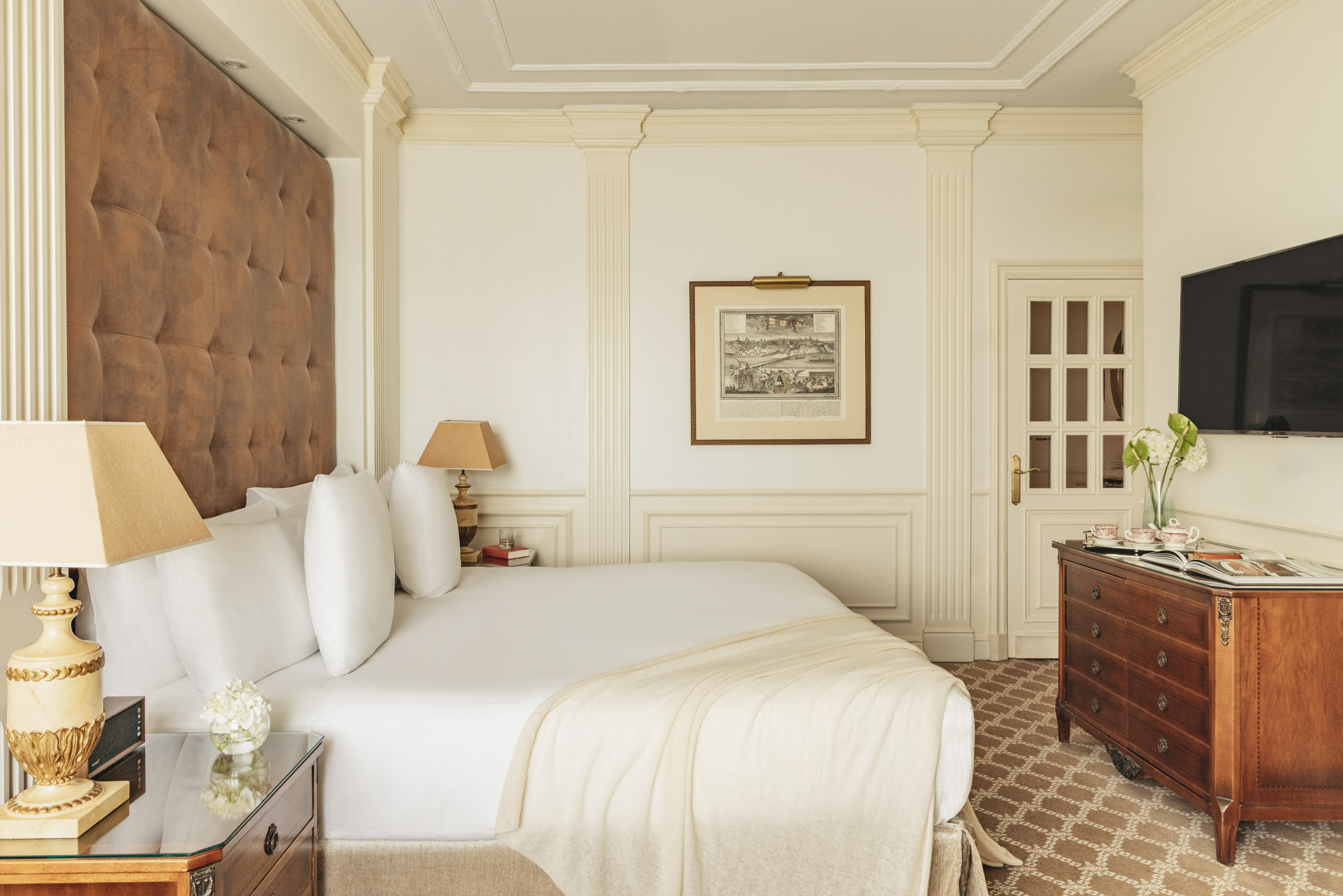 Elegant hotel bedroom with tufted headboard, white bed, classic wooden dresser.