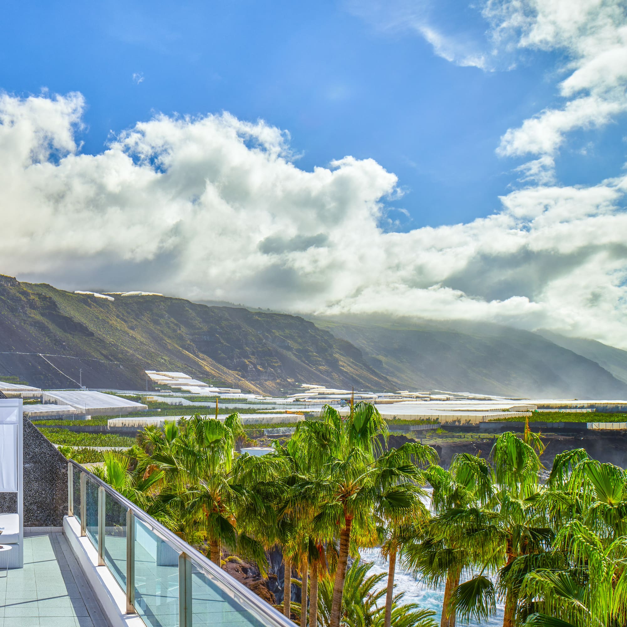 a balcony with palm trees and mountains in the background