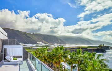 a balcony with palm trees and mountains in the background