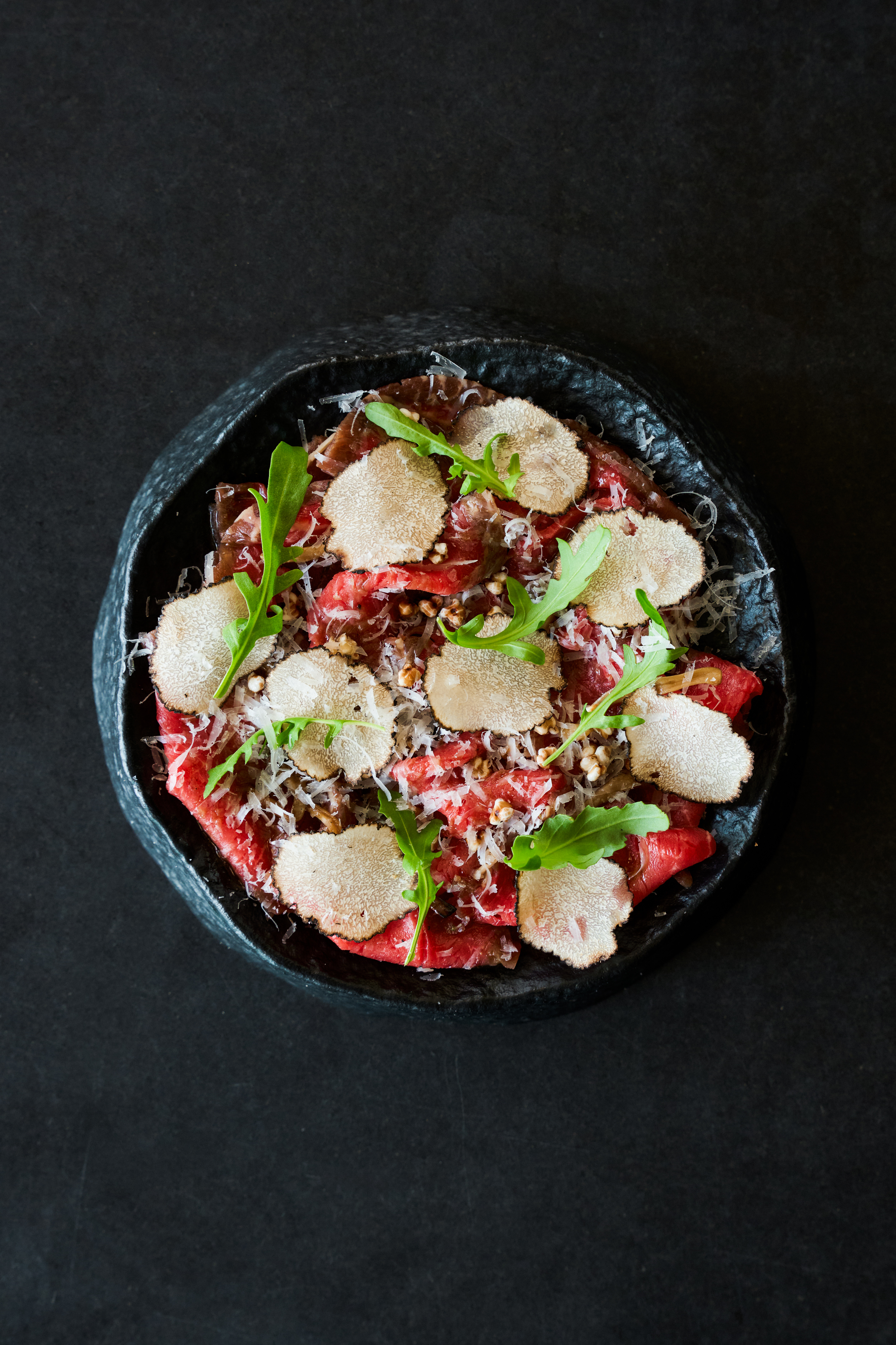 Gourmet beef carpaccio with white truffle, Parmesan, arugula on dark plate.