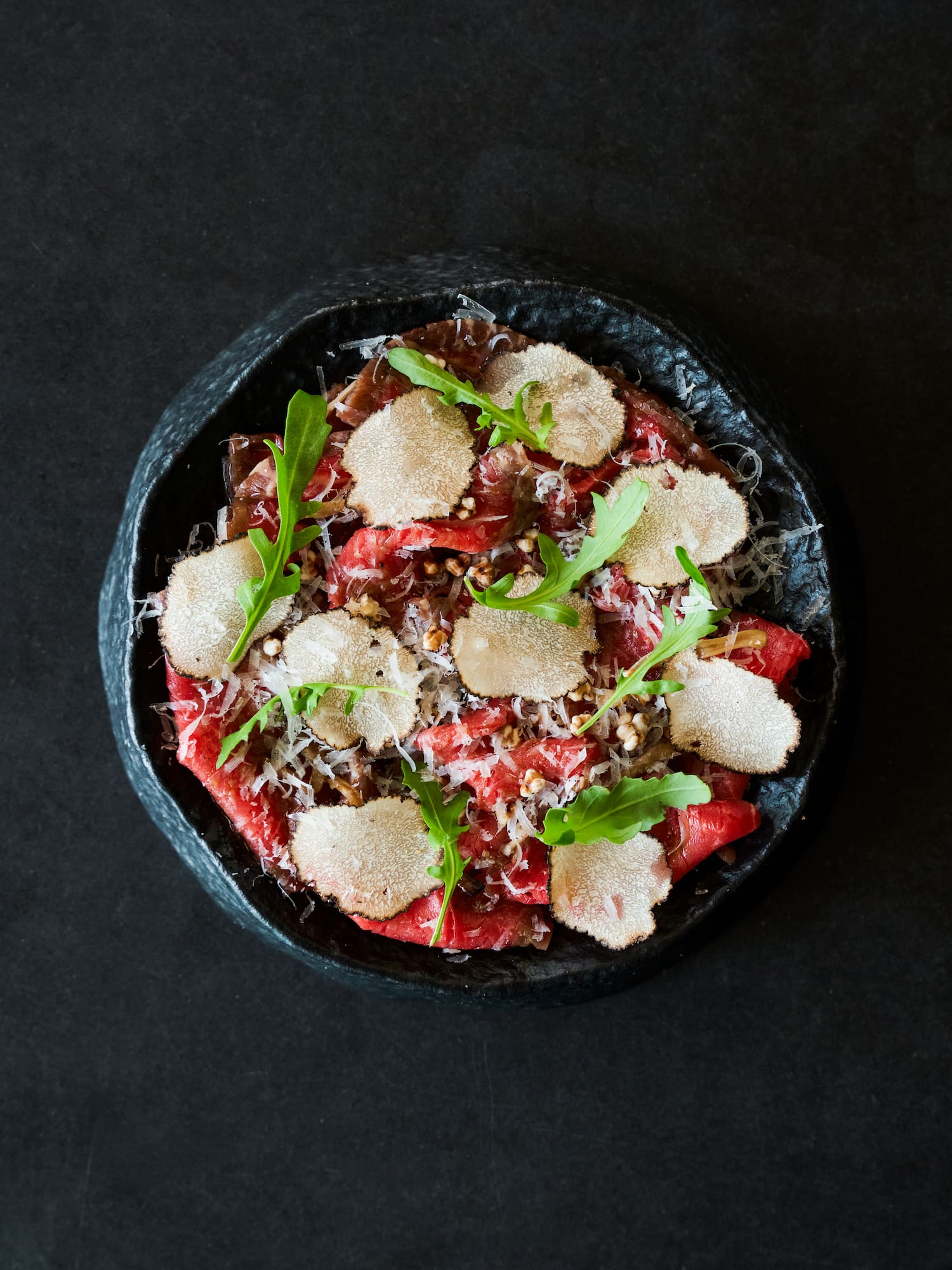 Gourmet beef carpaccio with white truffle, Parmesan, arugula on dark plate.