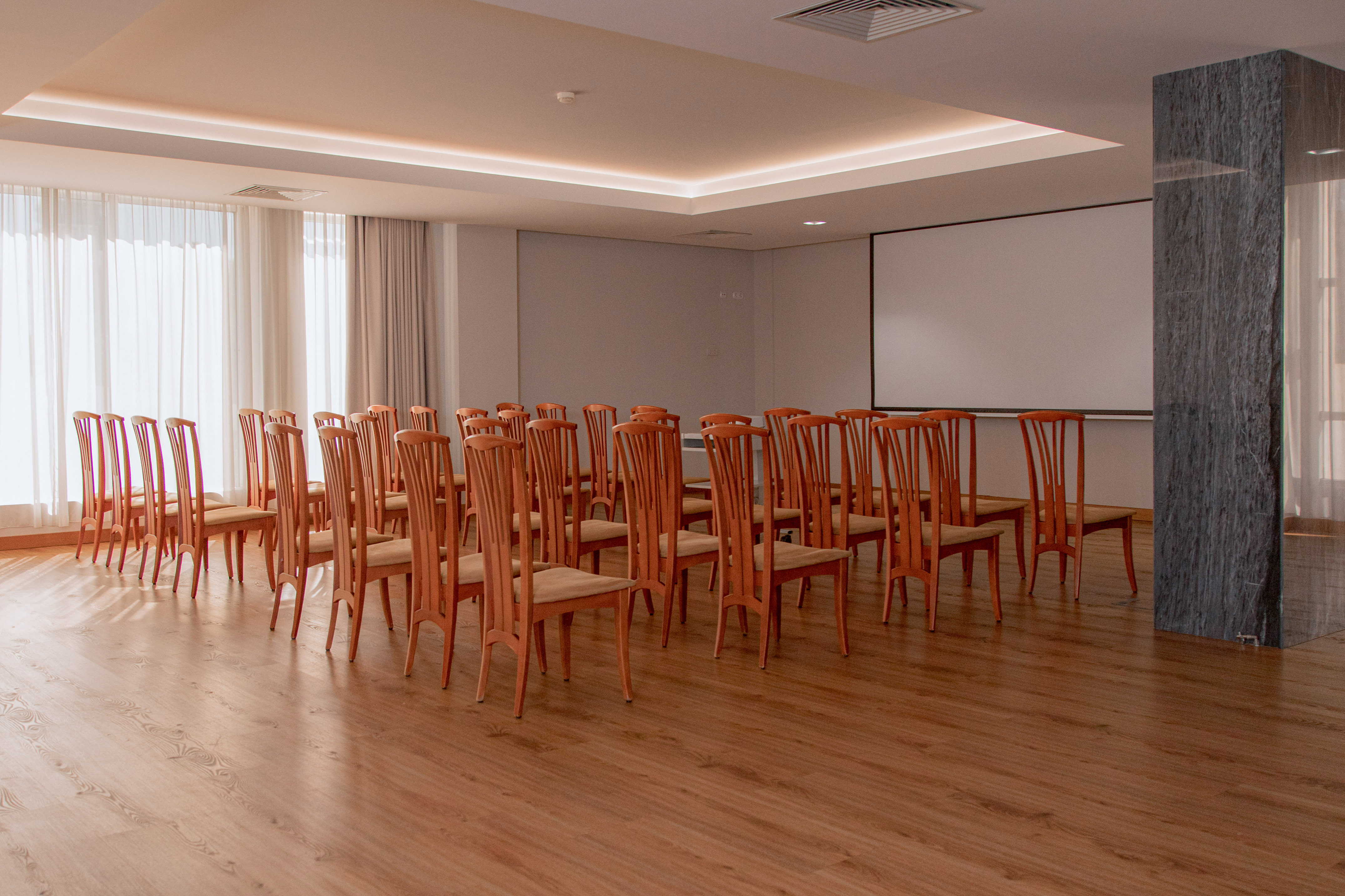 Empty conference room with wooden chairs, projector screen, and light wood floor.
