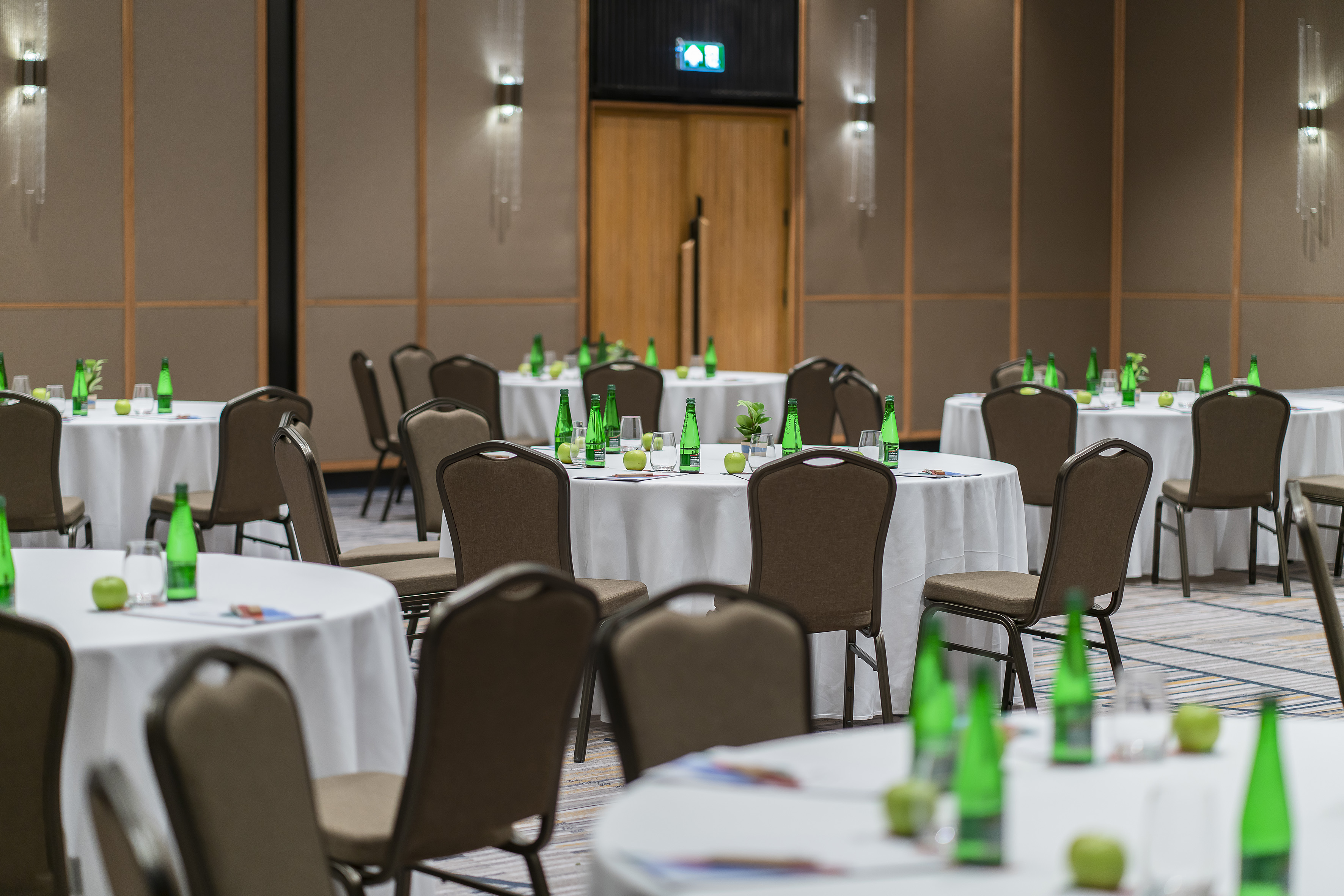Prepared meeting room with round tables, chairs, water bottles, and apples.