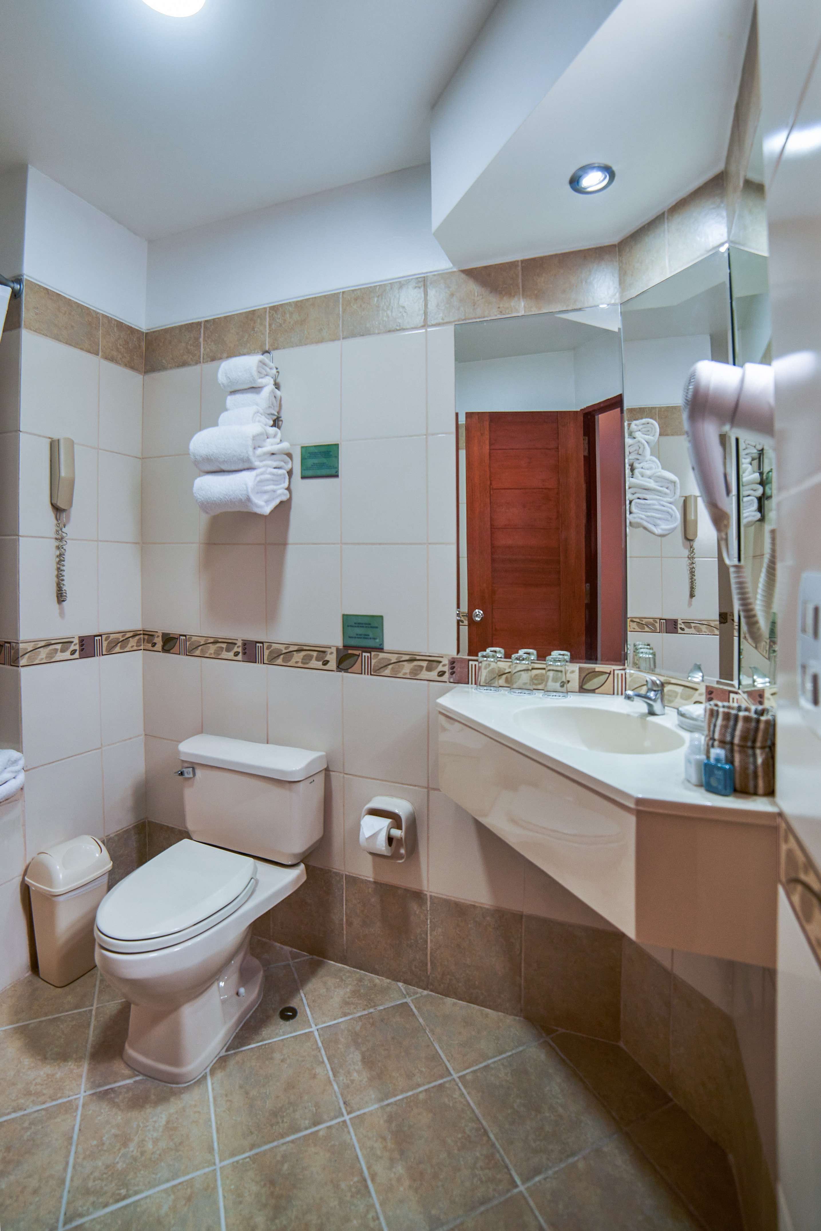 Hotel bathroom with neutral tiles, toilet, sink vanity, mirror, and white towels.