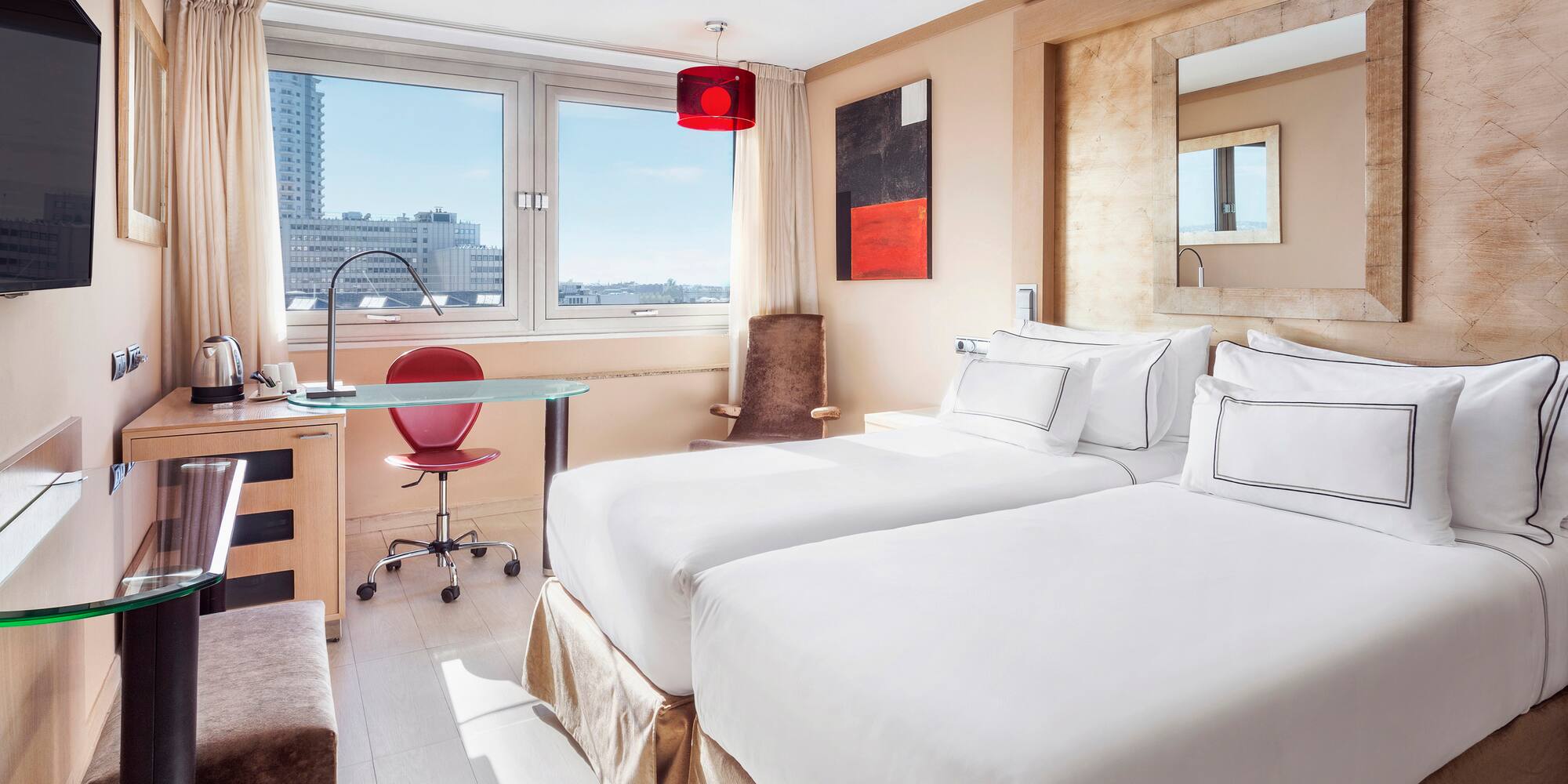 Modern hotel room with twin beds, city view window, desk, and red accents.