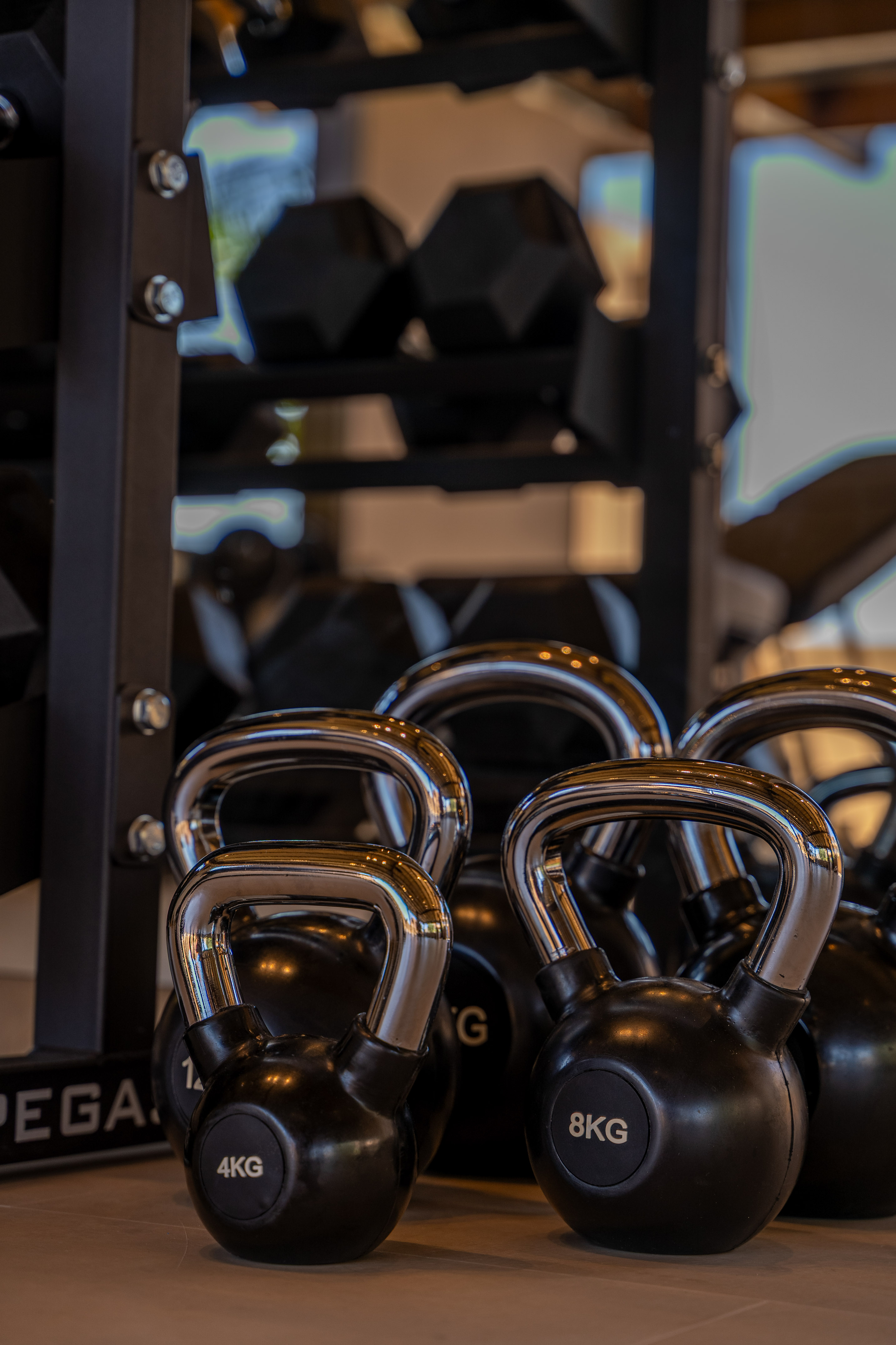 Black kettlebells (4kg, 8kg) on gym floor, with dumbbells rack.