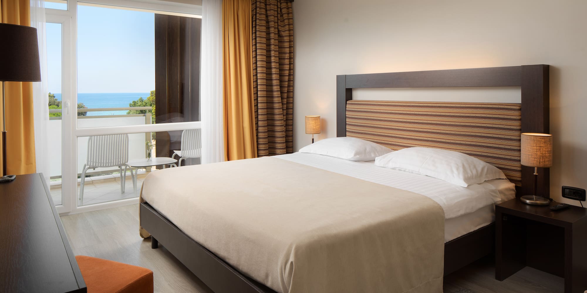 a bed with a wood headboard and a chair in a room with a view of the ocean