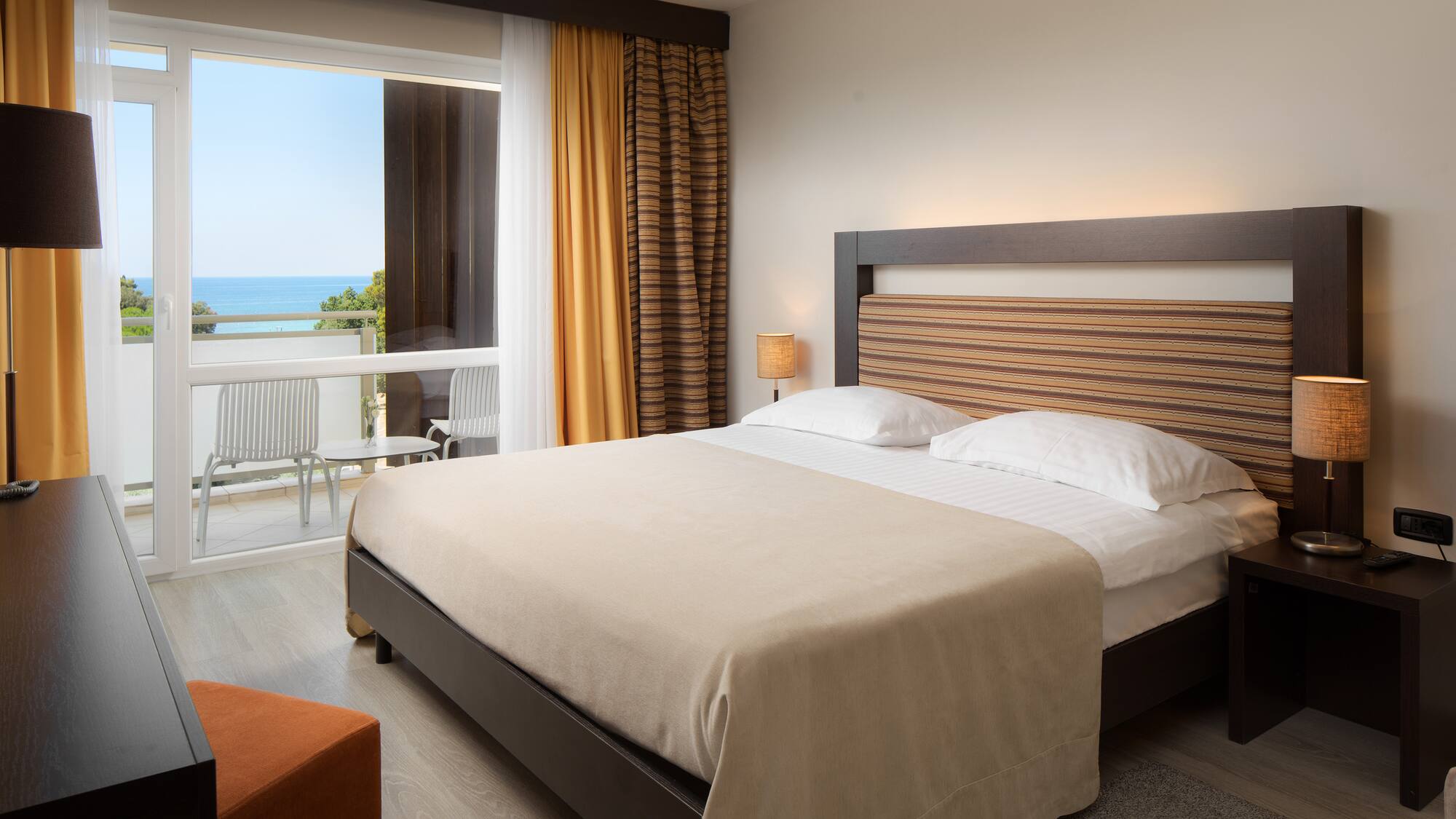 a bed with a wood headboard and a chair in a room with a view of the ocean