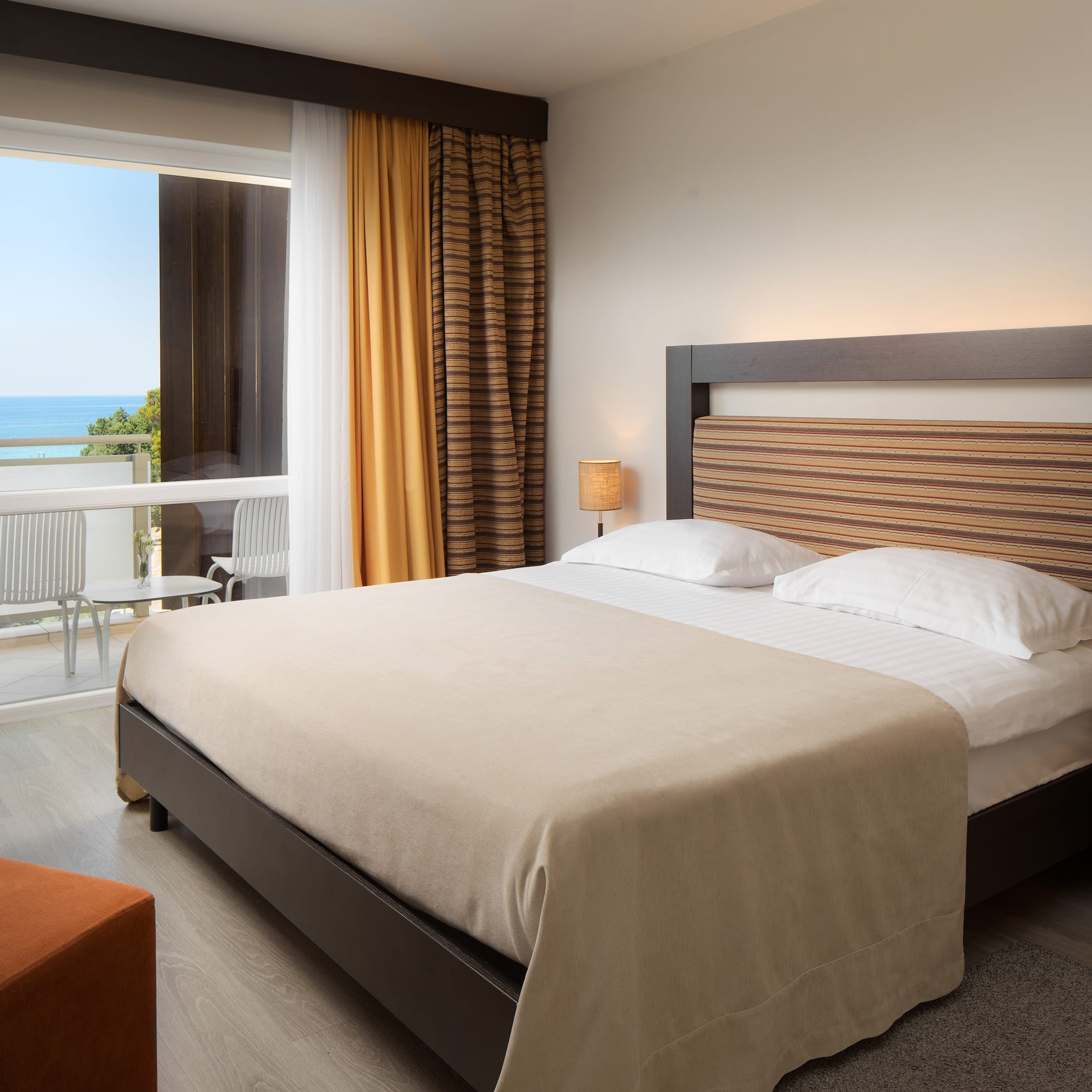 a bed with a wood headboard and a chair in a room with a view of the ocean