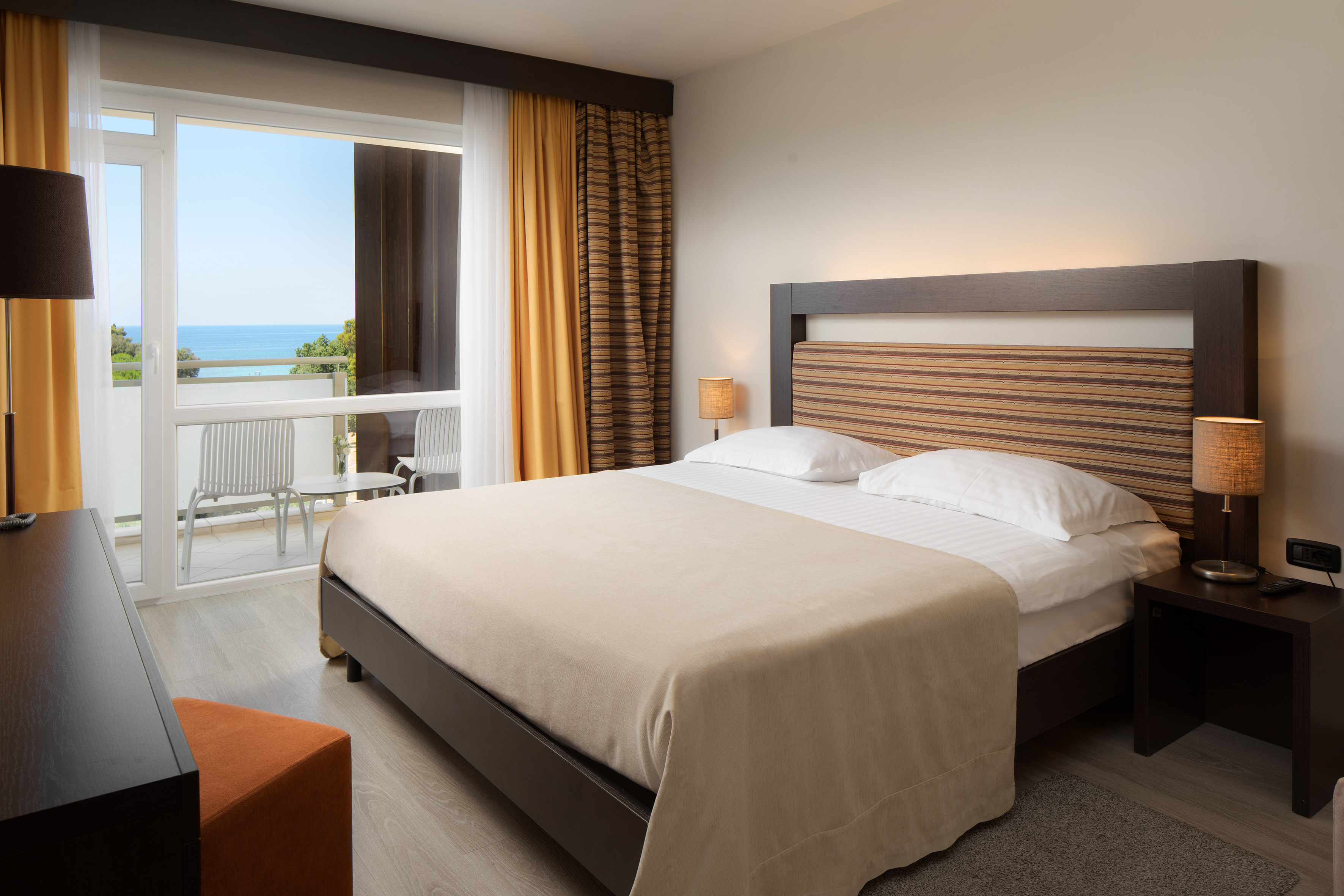 a bed with a wood headboard and a chair in a room with a view of the ocean