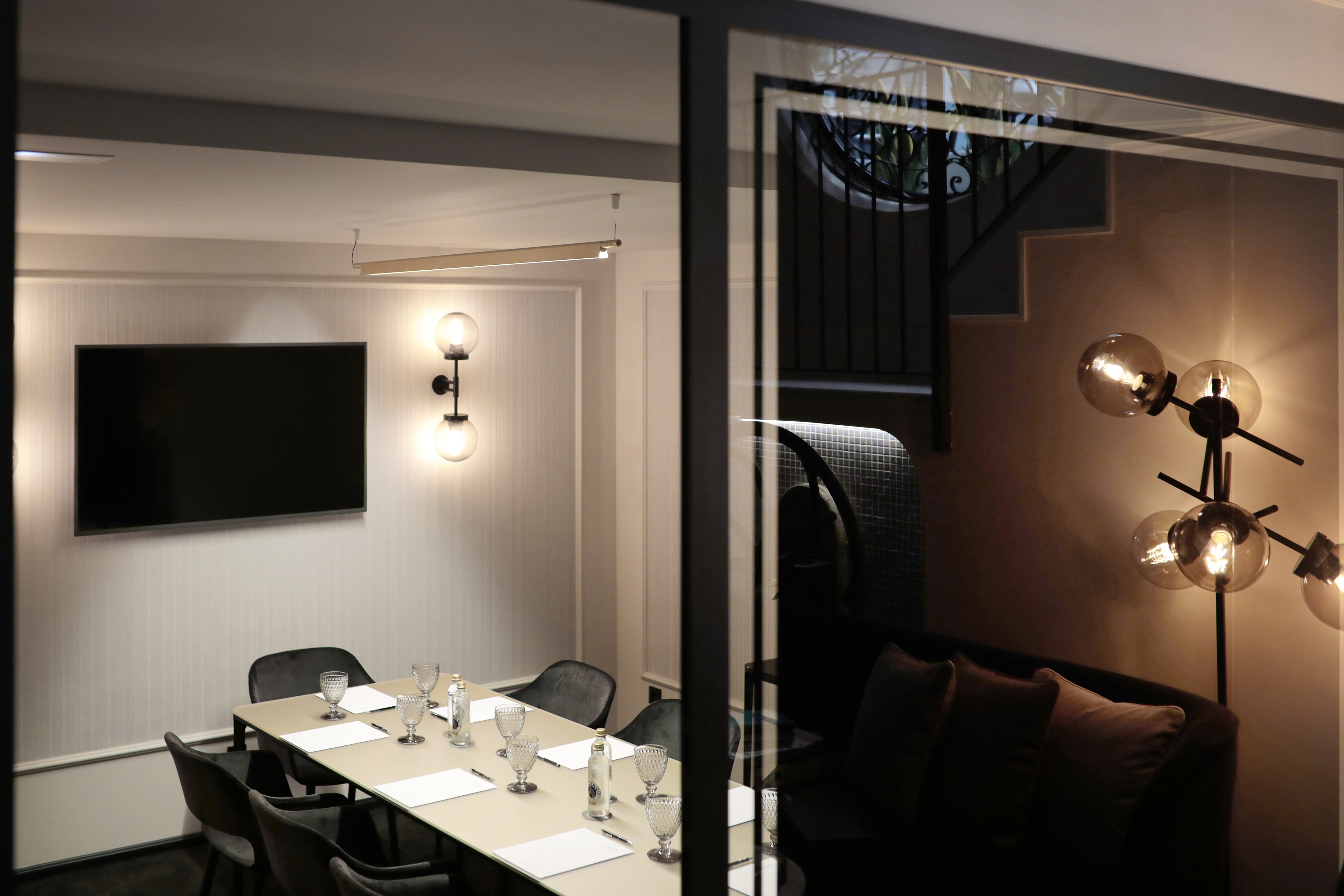 Modern conference room with TV and table, glass partition to lounge.