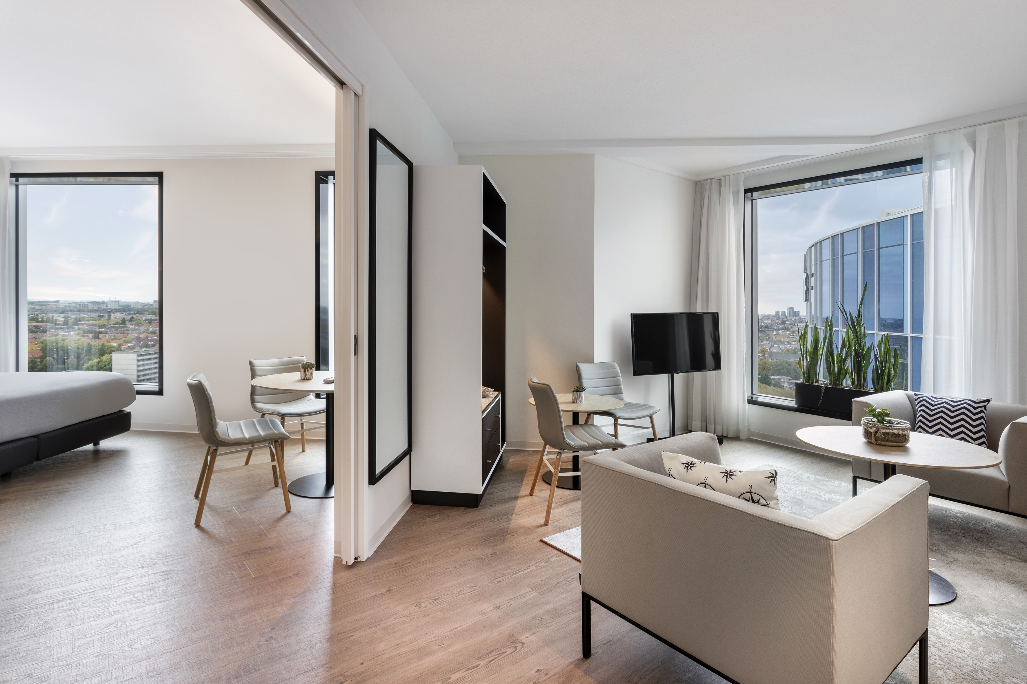 Modern hotel suite with living room, bedroom, wood flooring, and city views.