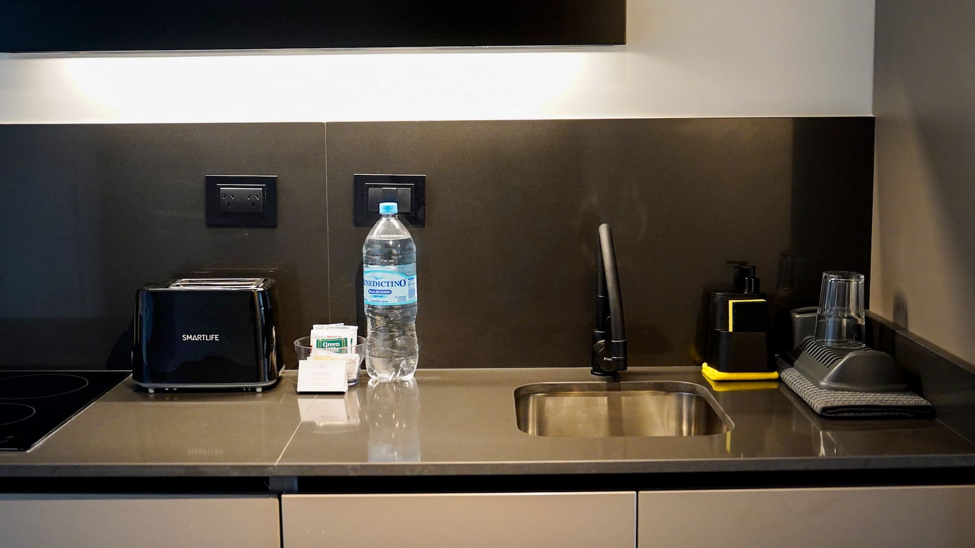 Modern hotel kitchenette with black toaster, sink, and water bottle.