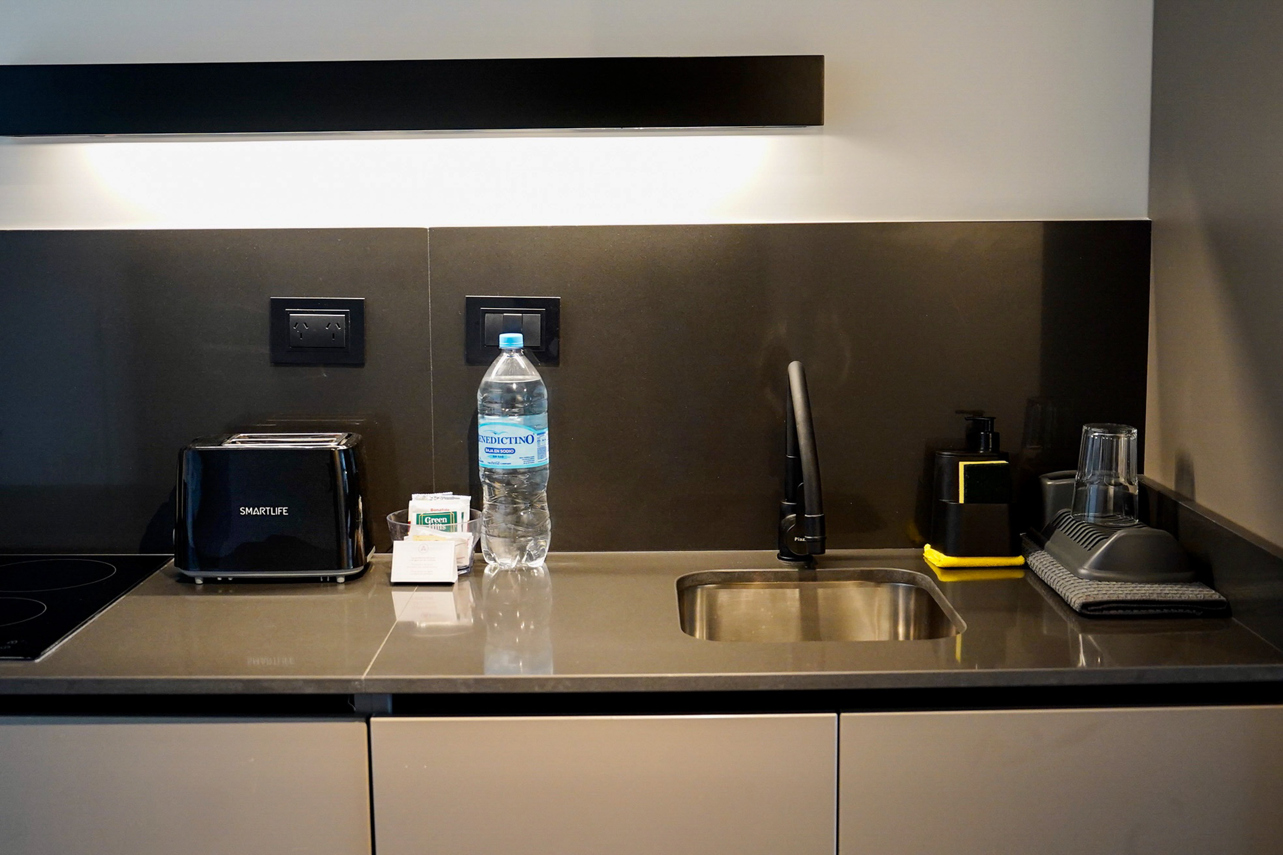 Modern hotel kitchenette with black toaster, sink, and water bottle.