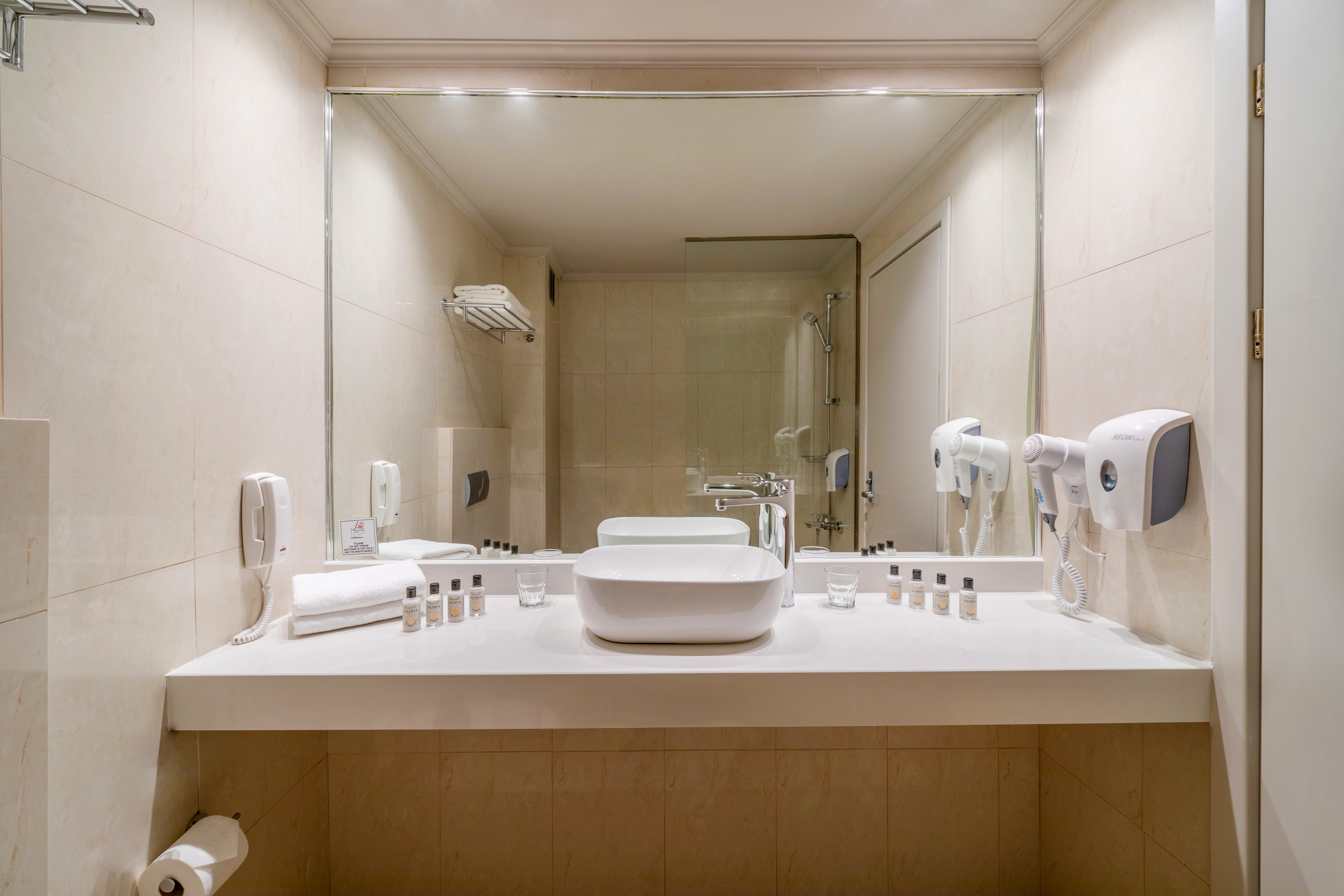 Modern hotel bathroom vanity with vessel sink, large mirror, and amenities.