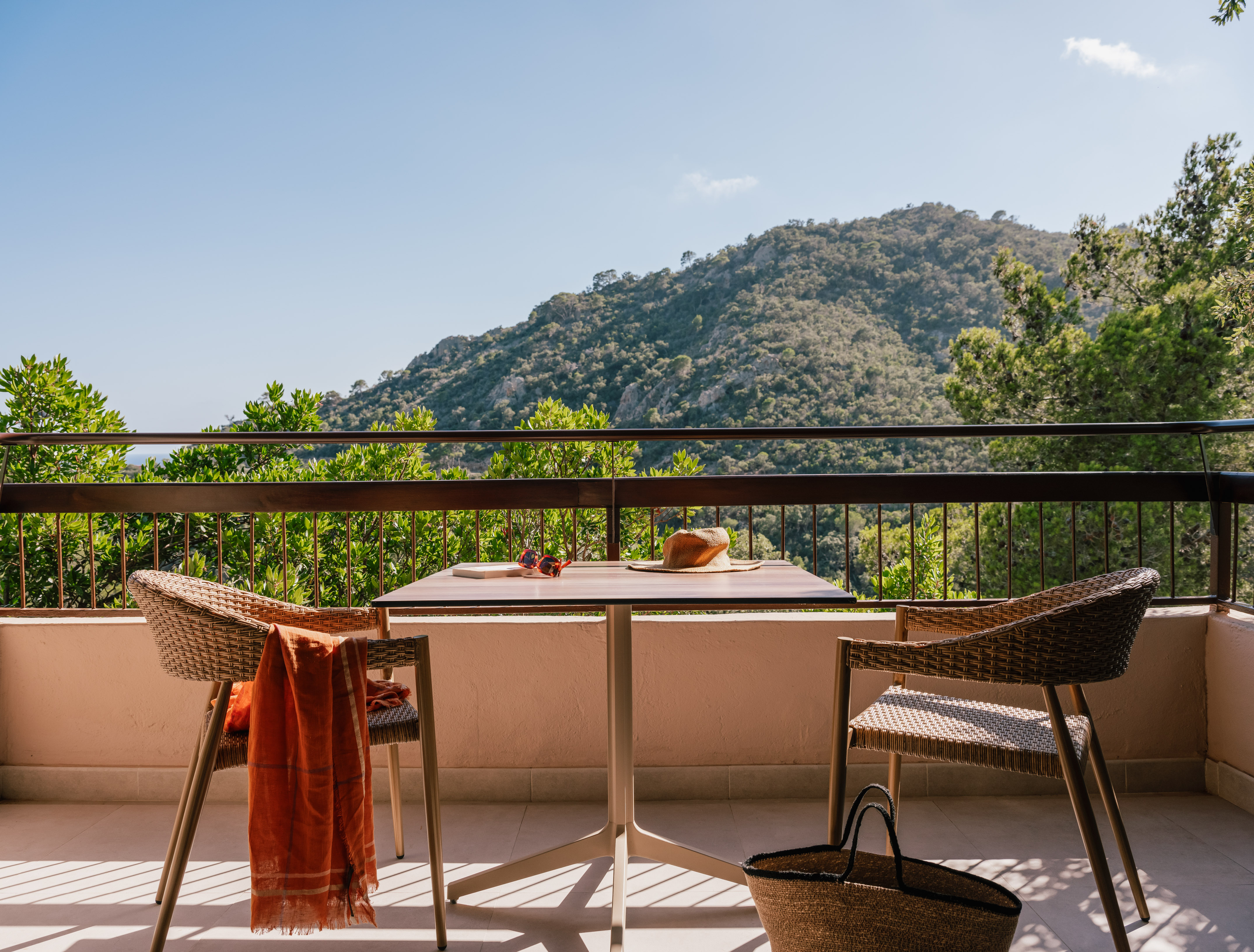 Balcony with mountain view, outdoor dining table, chairs, hat and sunglasses.