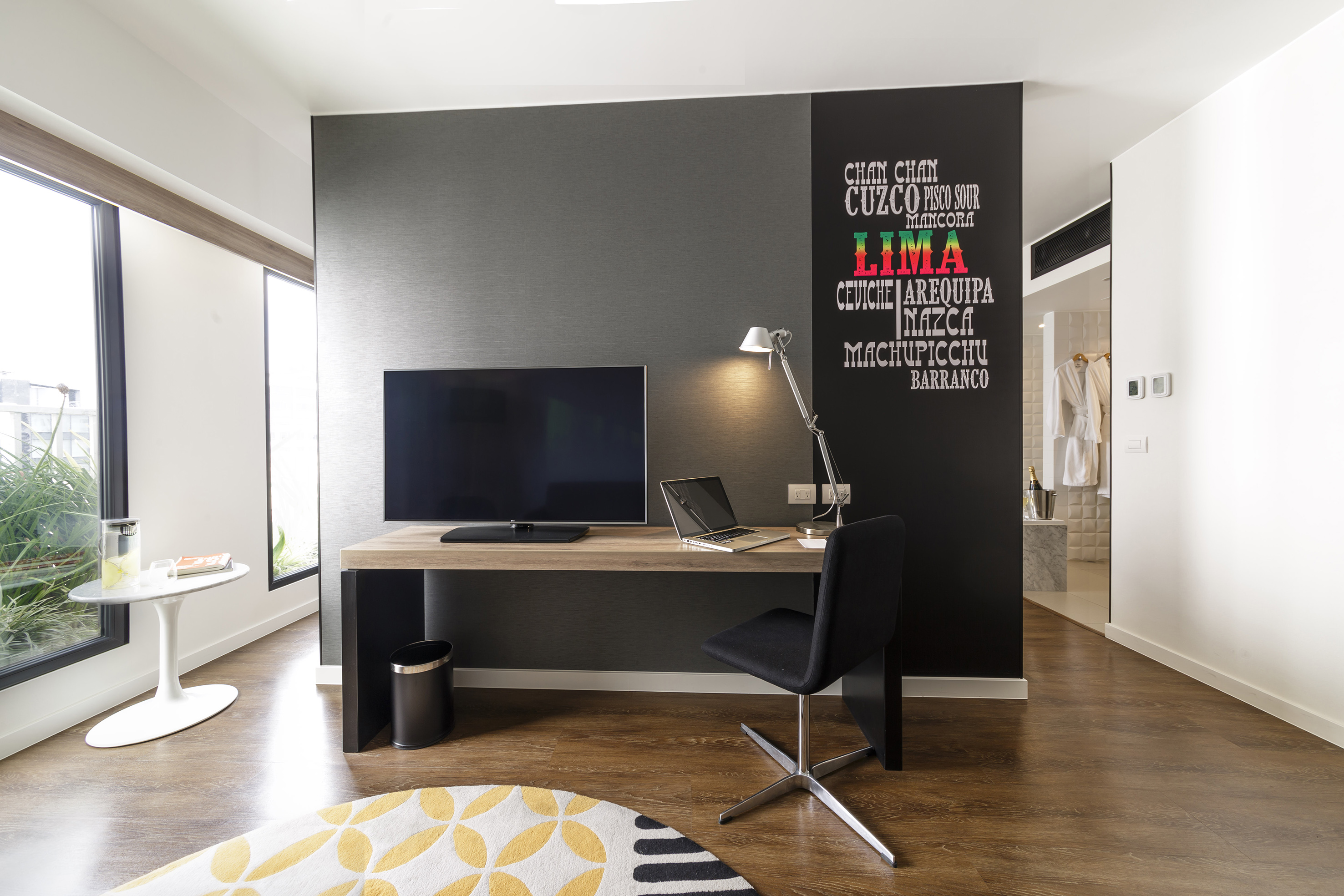 Modern hotel room workspace with TV, laptop, and Lima, Peru wall art.