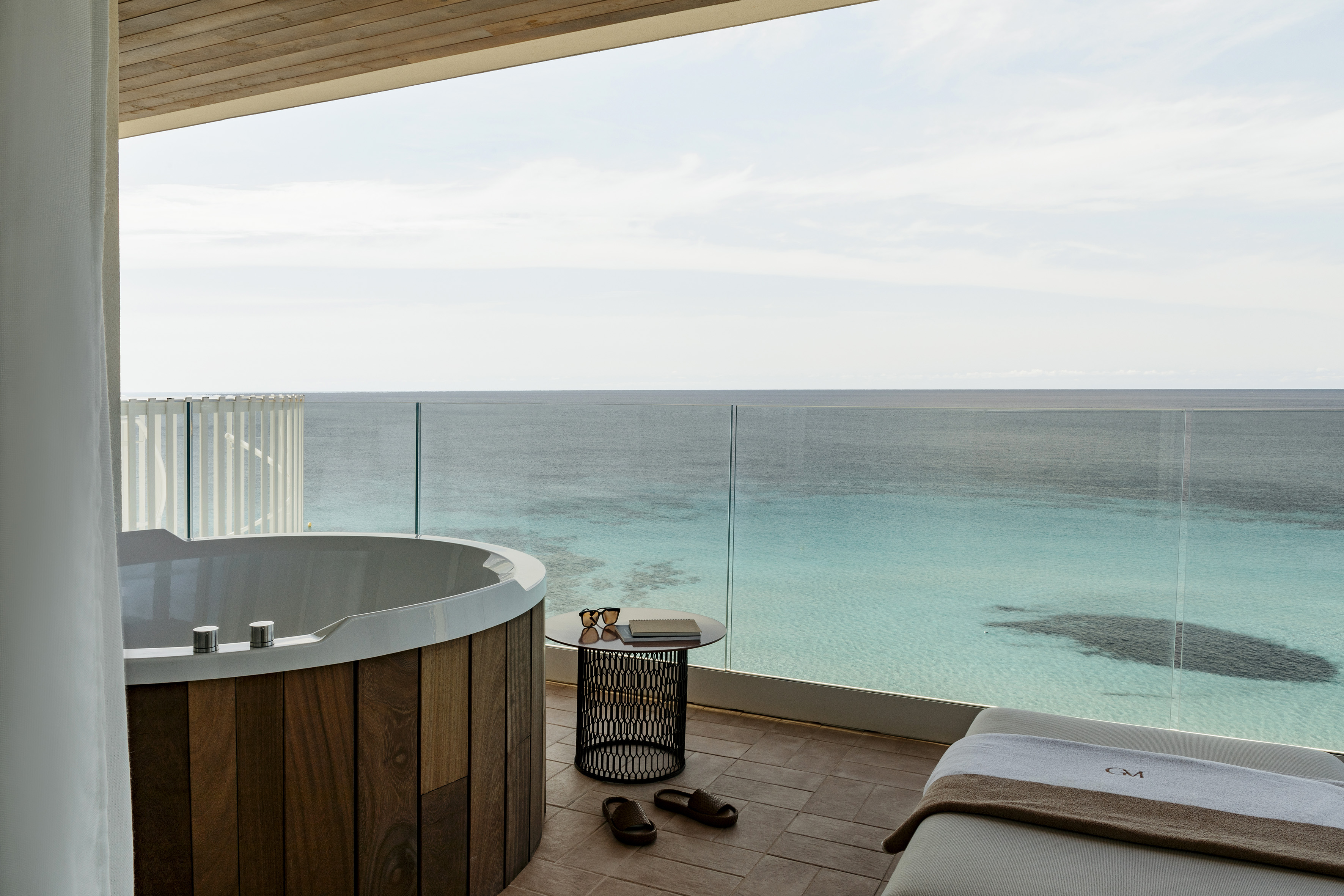 Tropical balcony with outdoor hot tub, lounge chair, and ocean view.