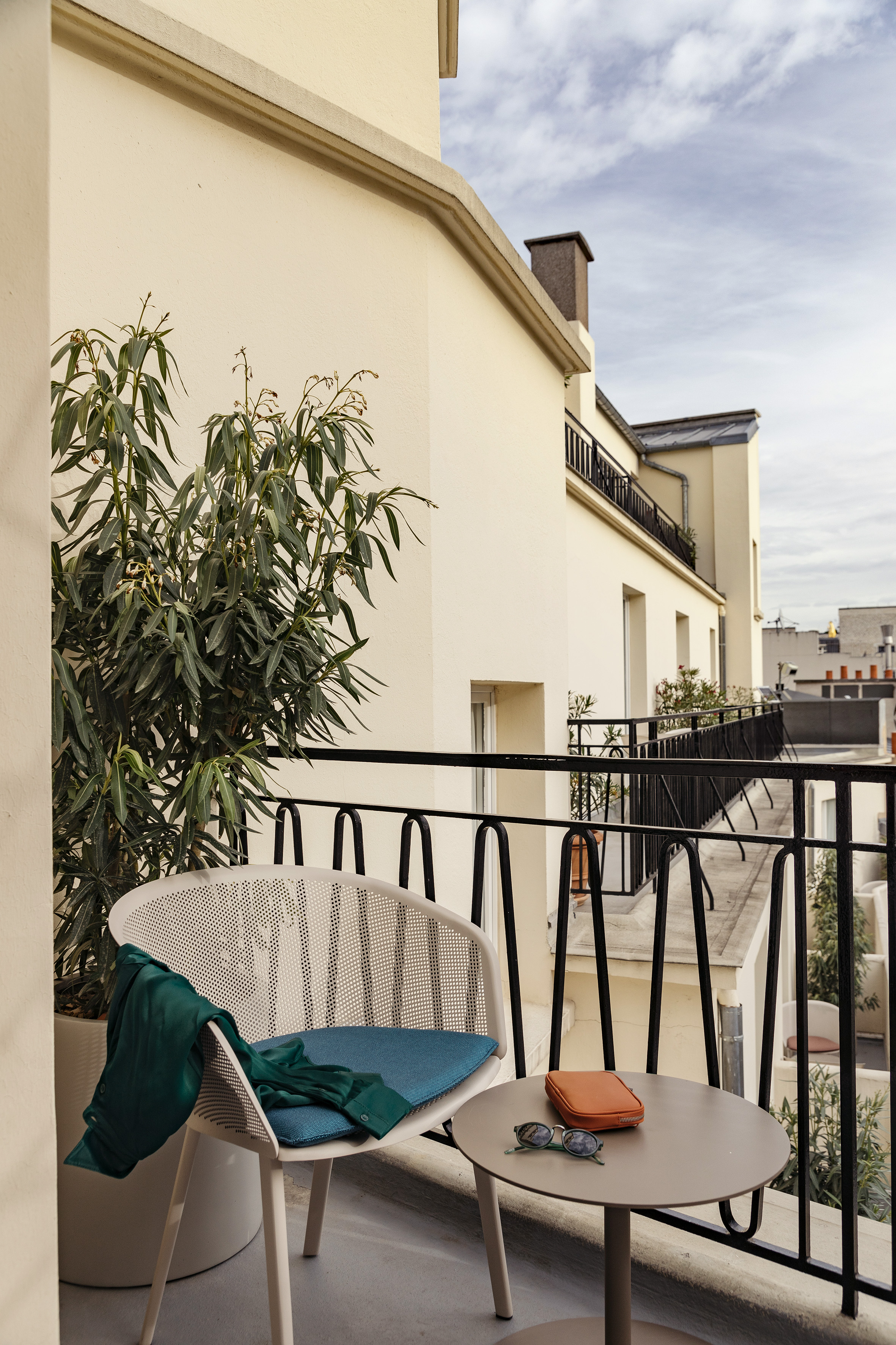 Modern hotel balcony with chair, plant, table, and cityscape view.