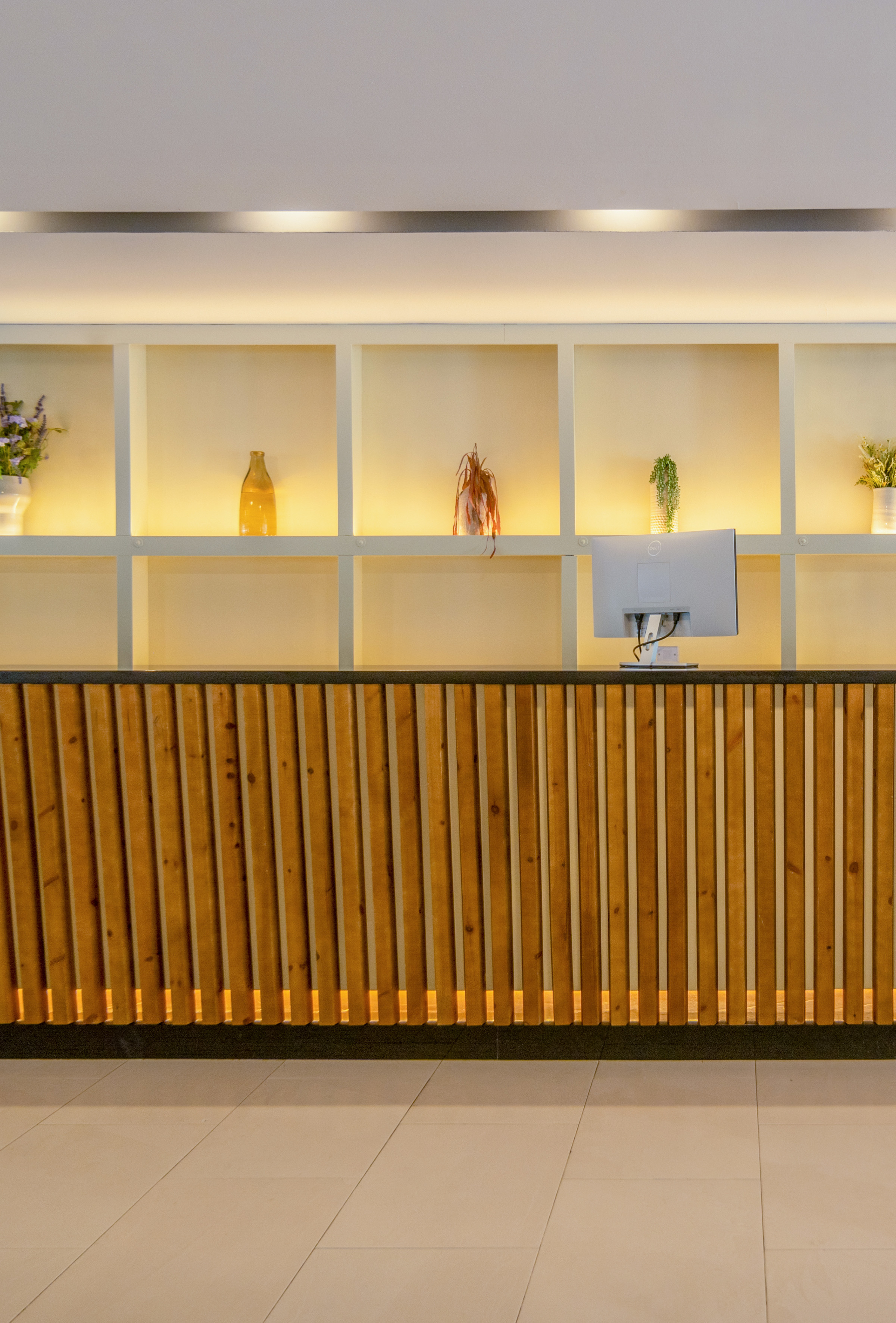 Hotel reception desk with wooden slatted counter, illuminated shelves, and monitor.
