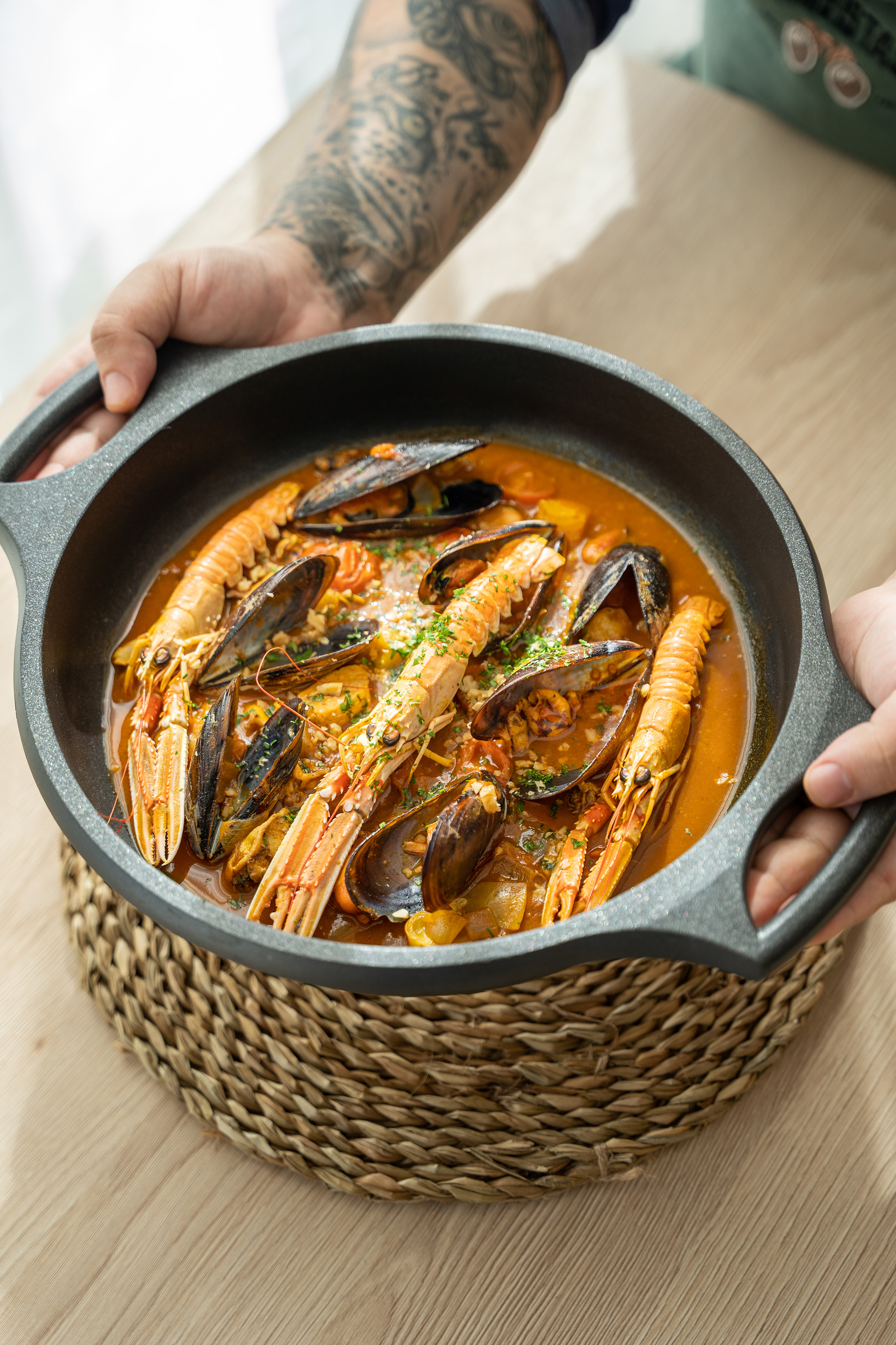 Hands holding cast iron skillet of seafood stew with mussels, langoustines.