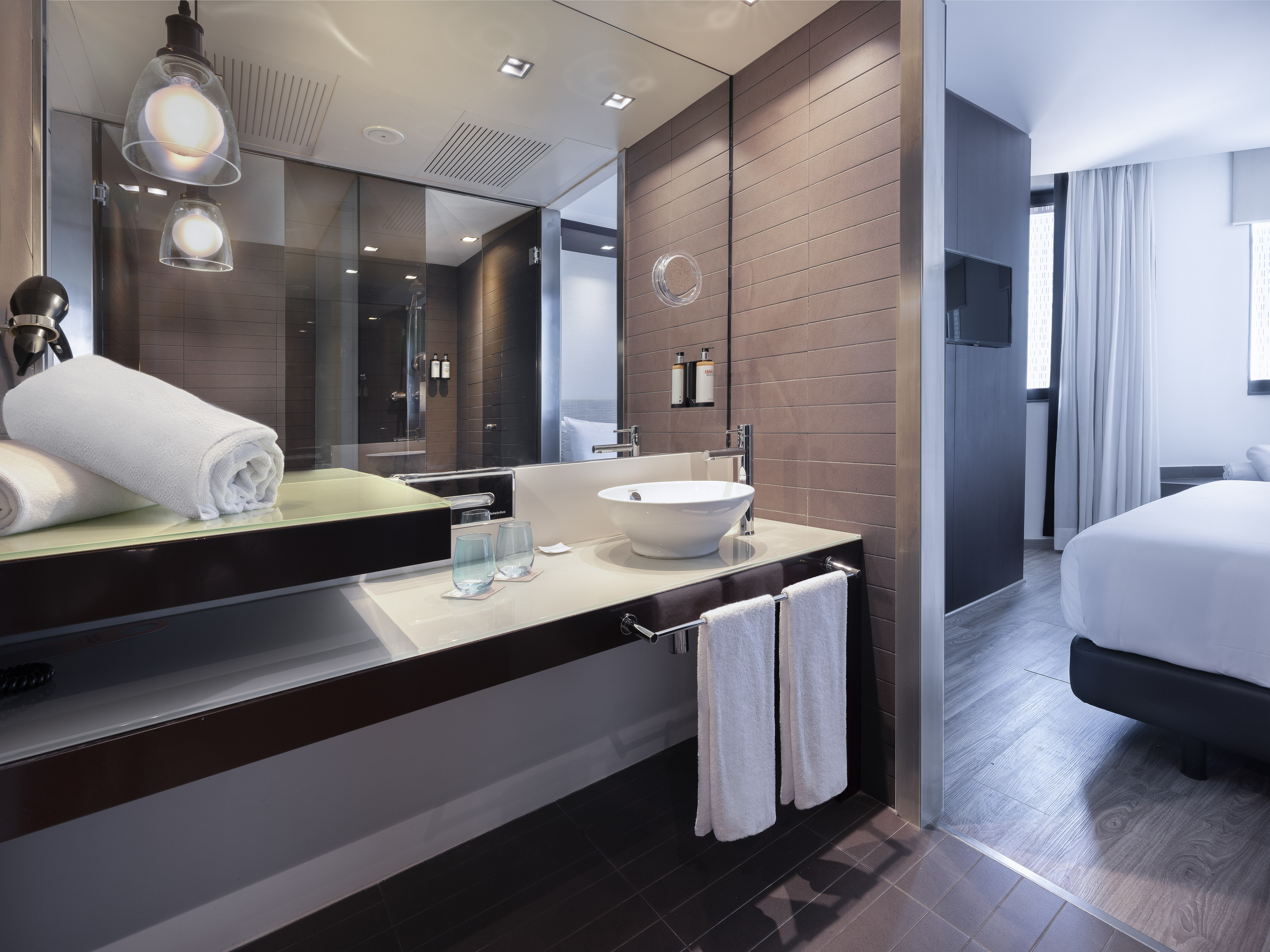 Modern hotel bathroom vanity with vessel sink, large mirror, and adjoining bedroom.
