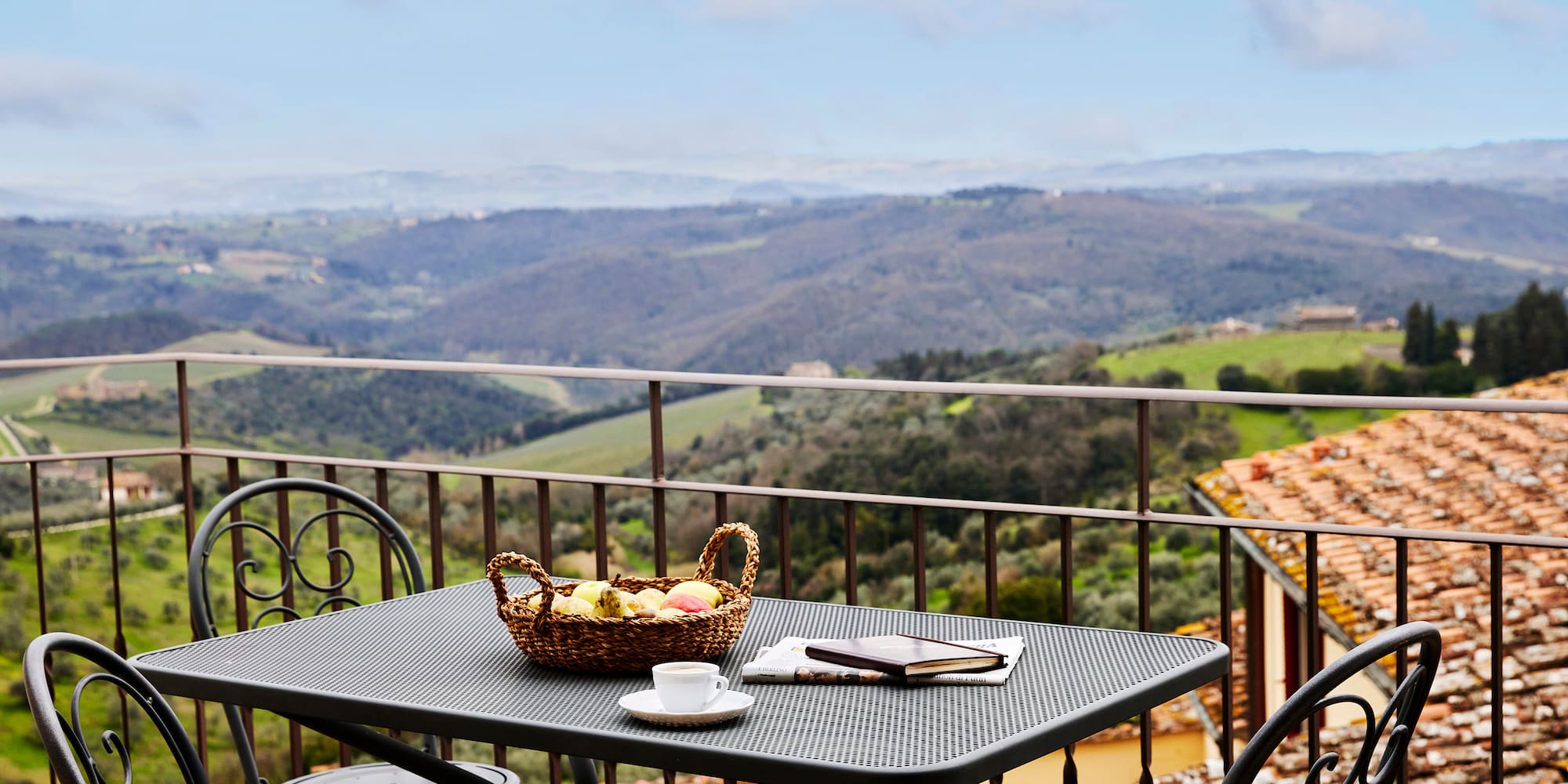 a table with a basket of fruit and a cup on a balcony overlooking a valley
