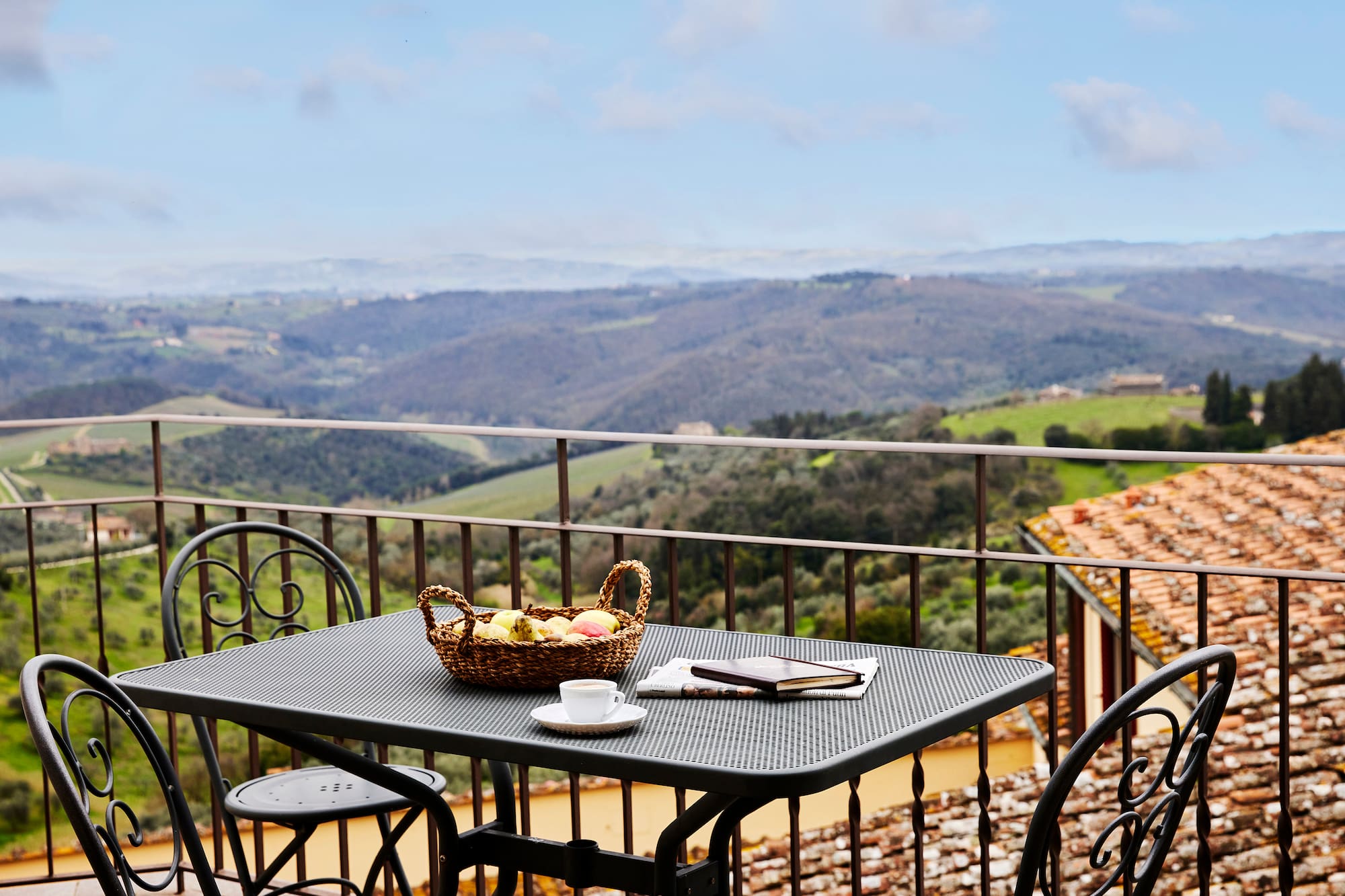 Balcony table with fruit, coffee, and book overlooking Tuscan hills.