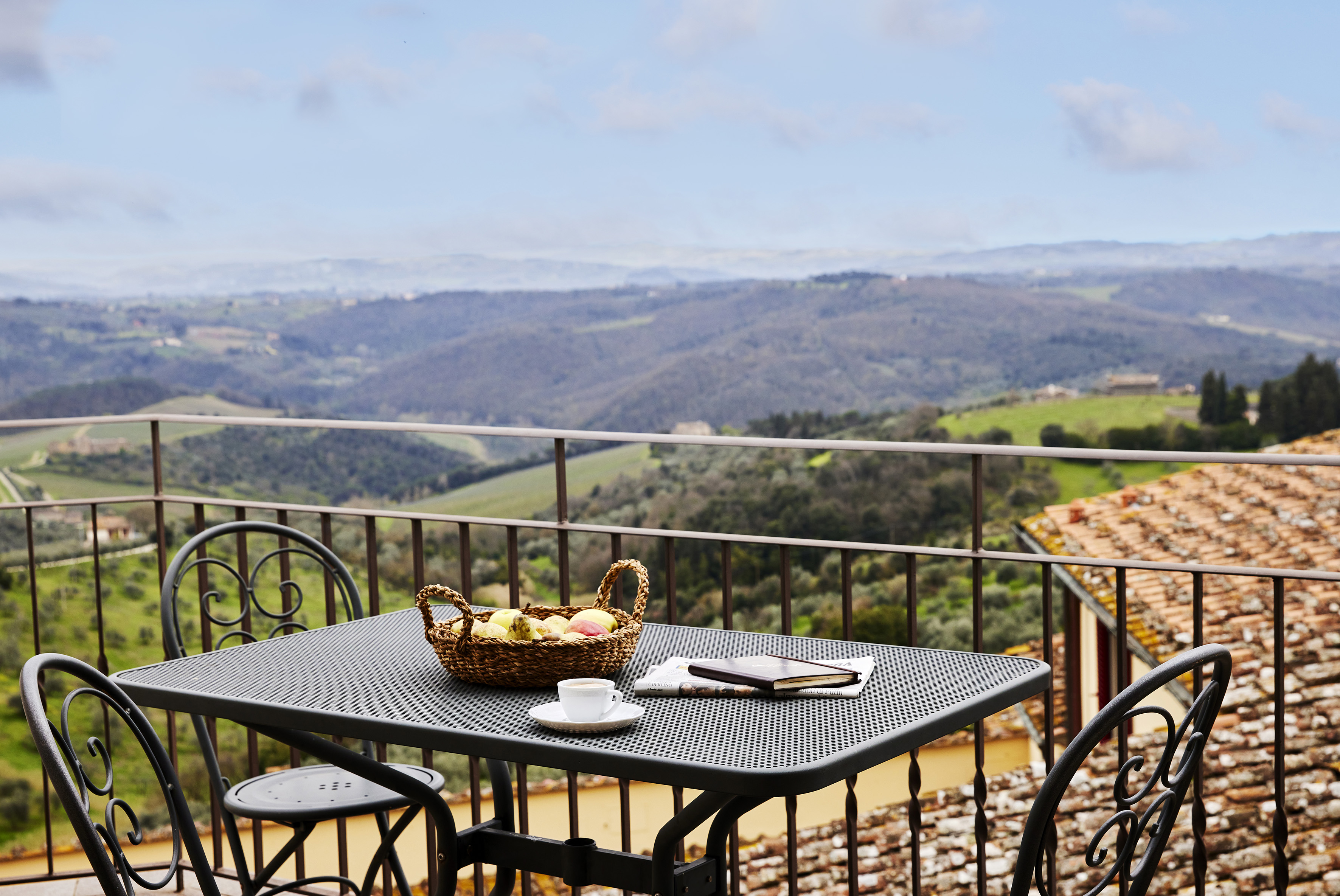a table with a basket of fruit and a cup on a balcony overlooking a valley