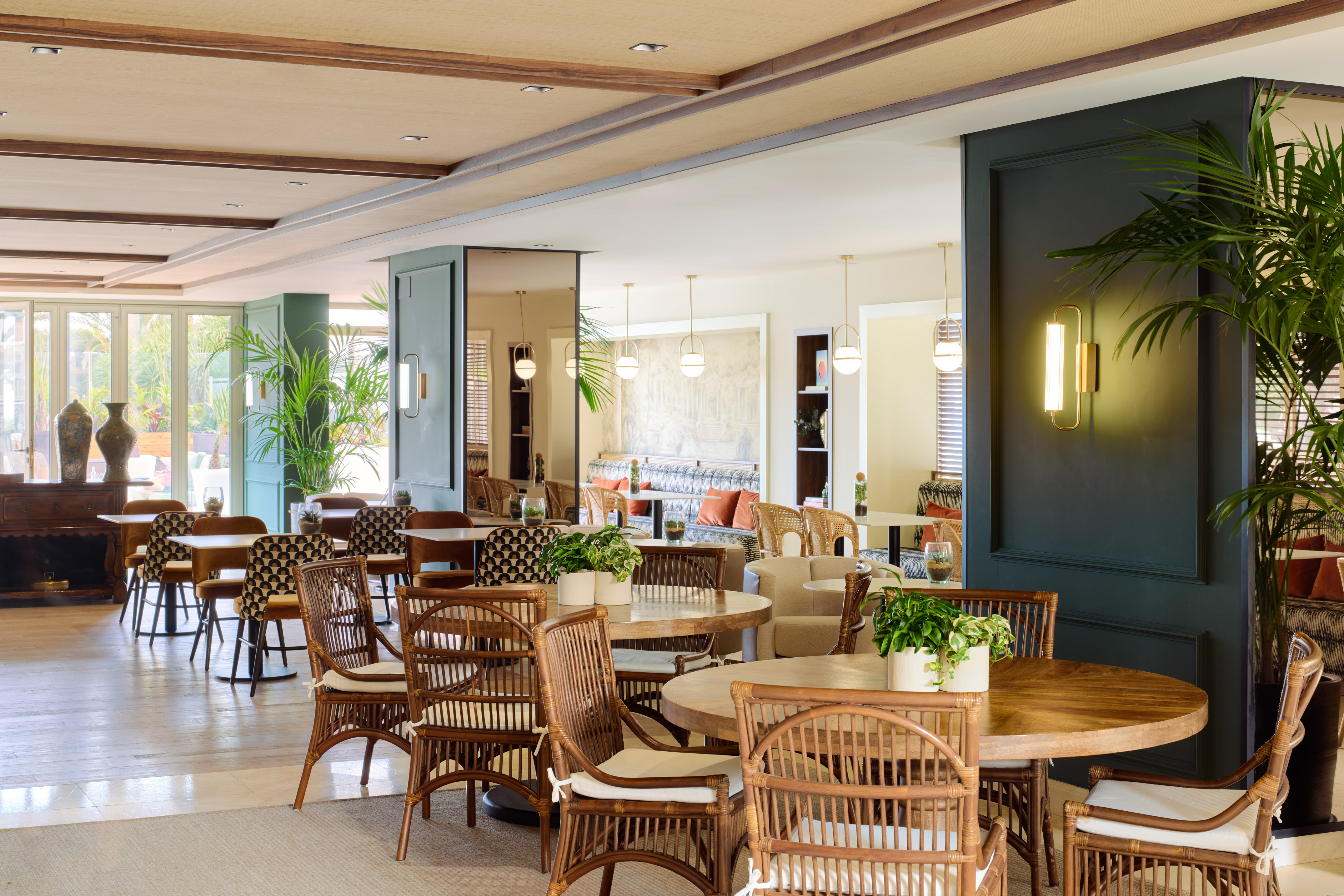 Modern hotel restaurant with rattan chairs, wooden tables, and green decor.