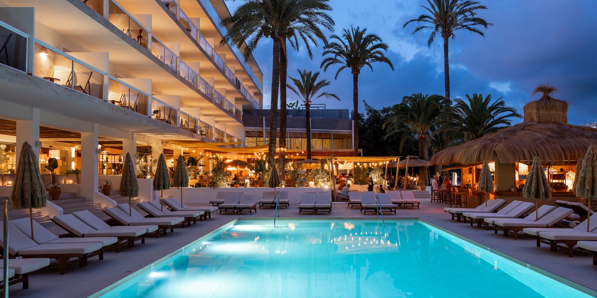 a pool with lounge chairs and palm trees in front of a building