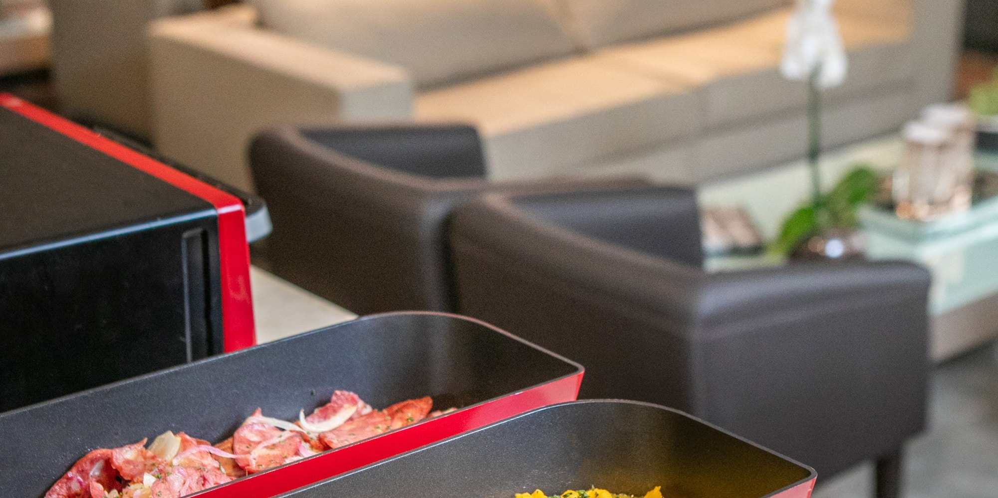 Hotel breakfast buffet: scrambled eggs, crispy bacon, ham in red dishes.