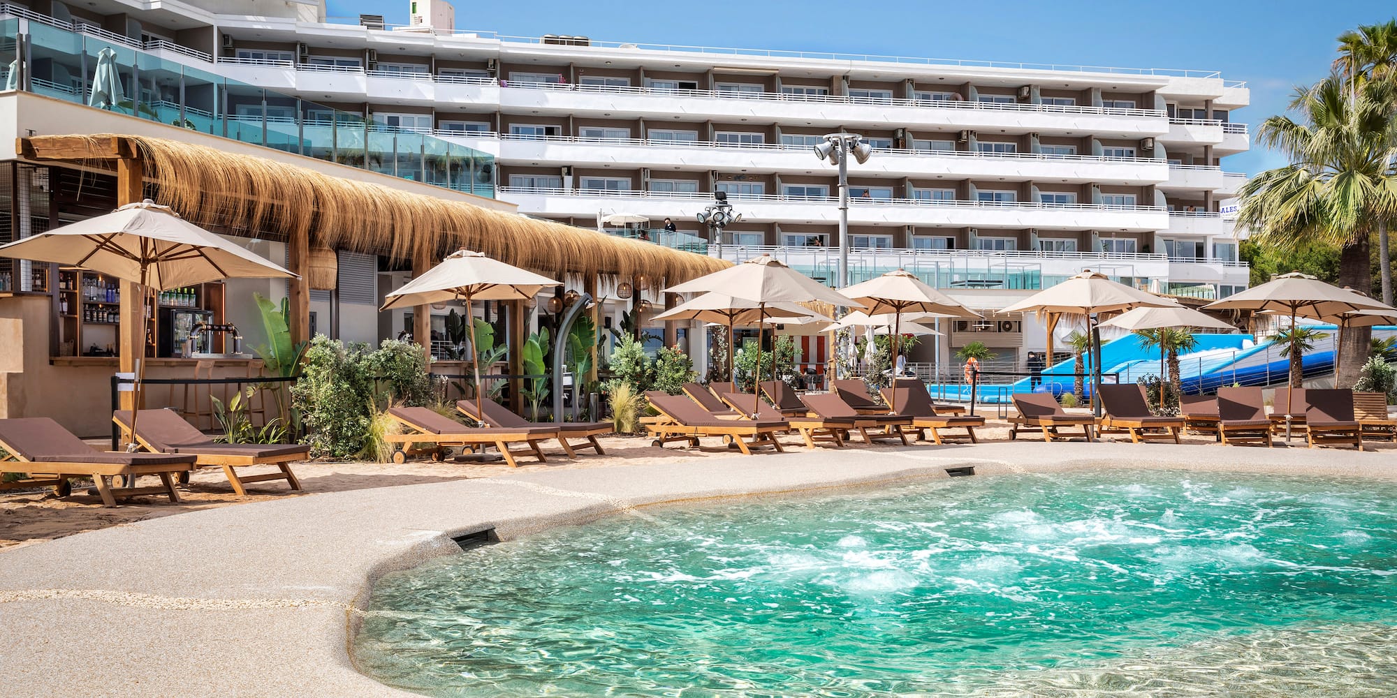 a pool with umbrellas and chairs in front of a hotel