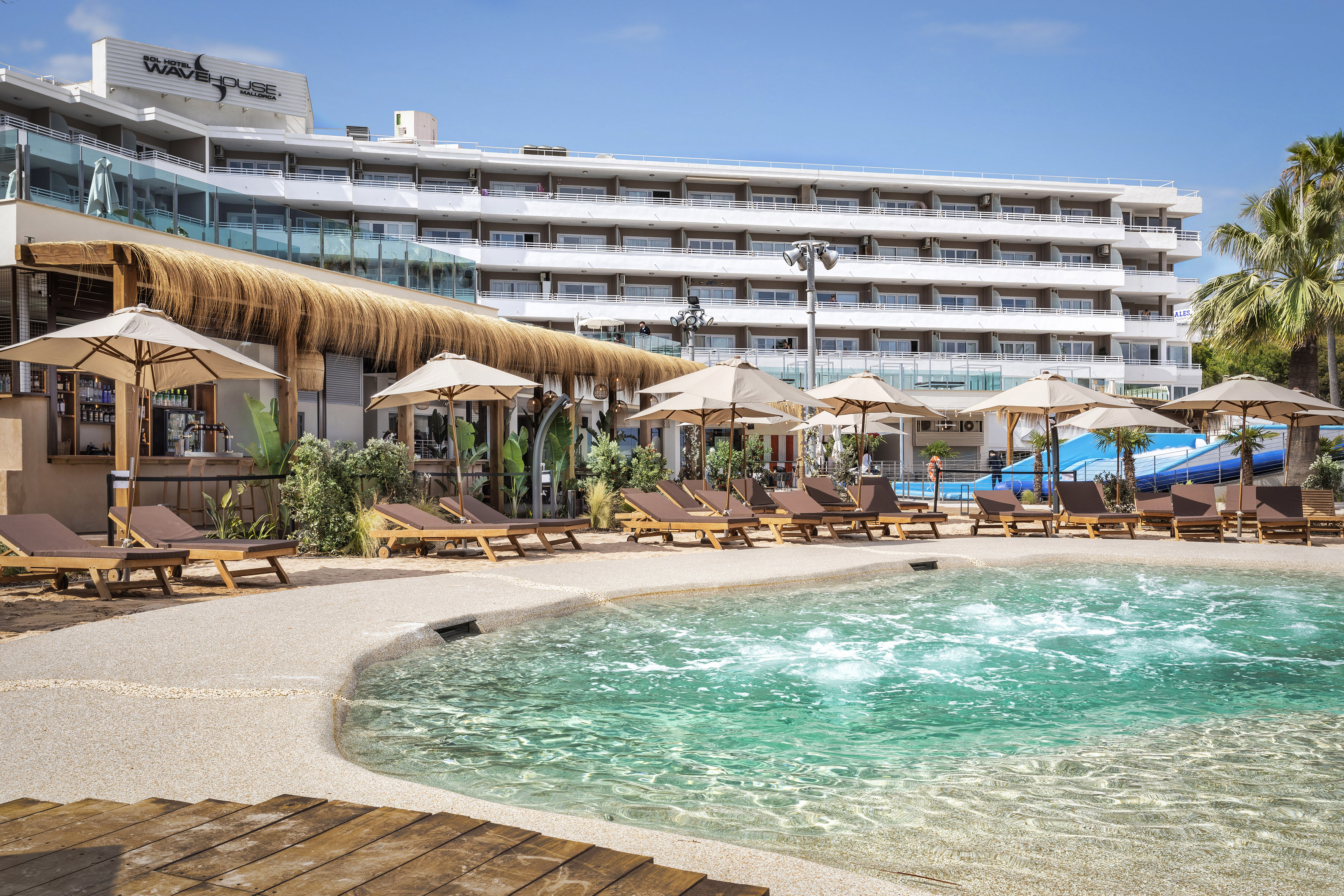 a pool with umbrellas and chairs in front of a hotel