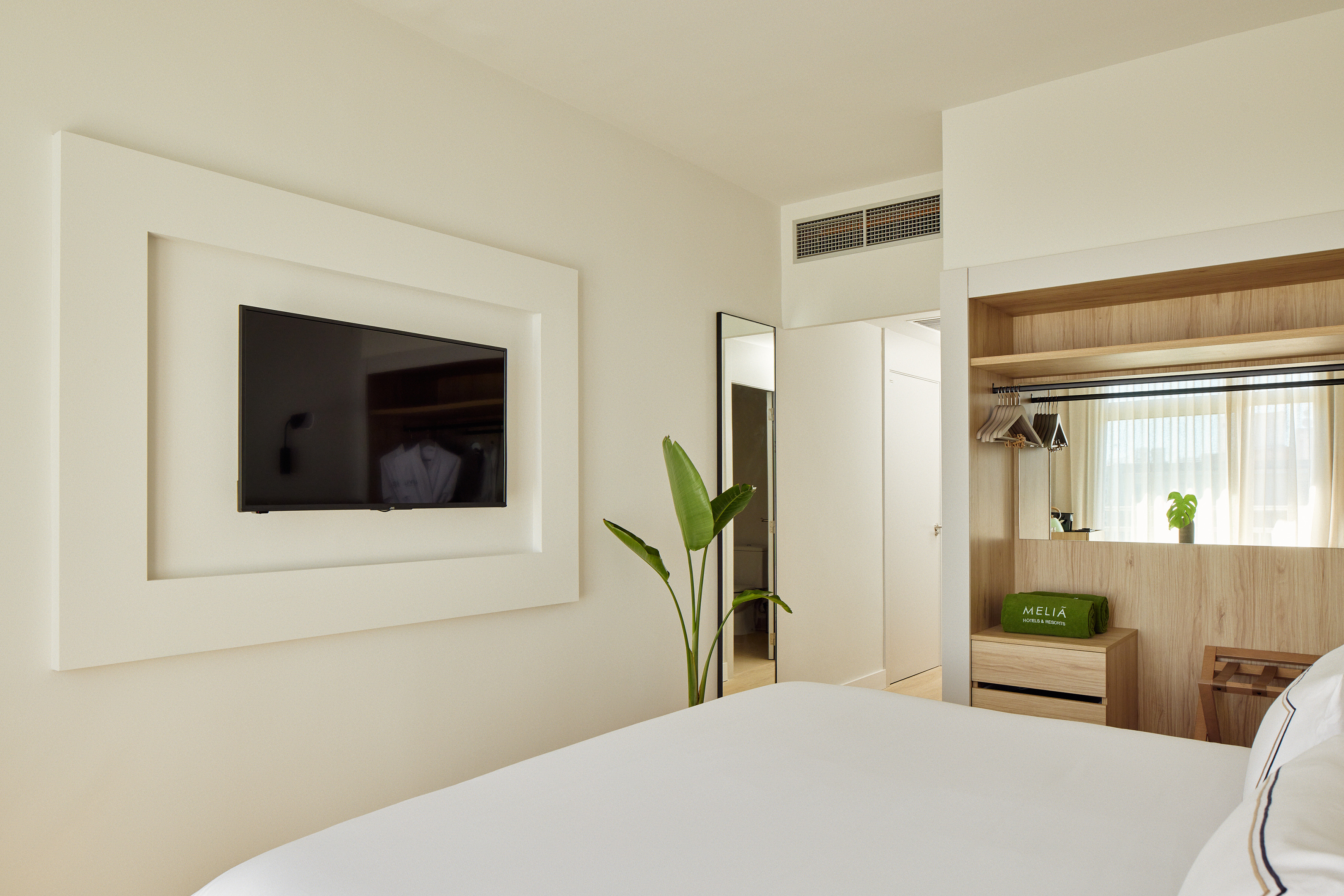 Modern Meliá hotel room with wall-mounted TV, white bed, and wooden wardrobe.