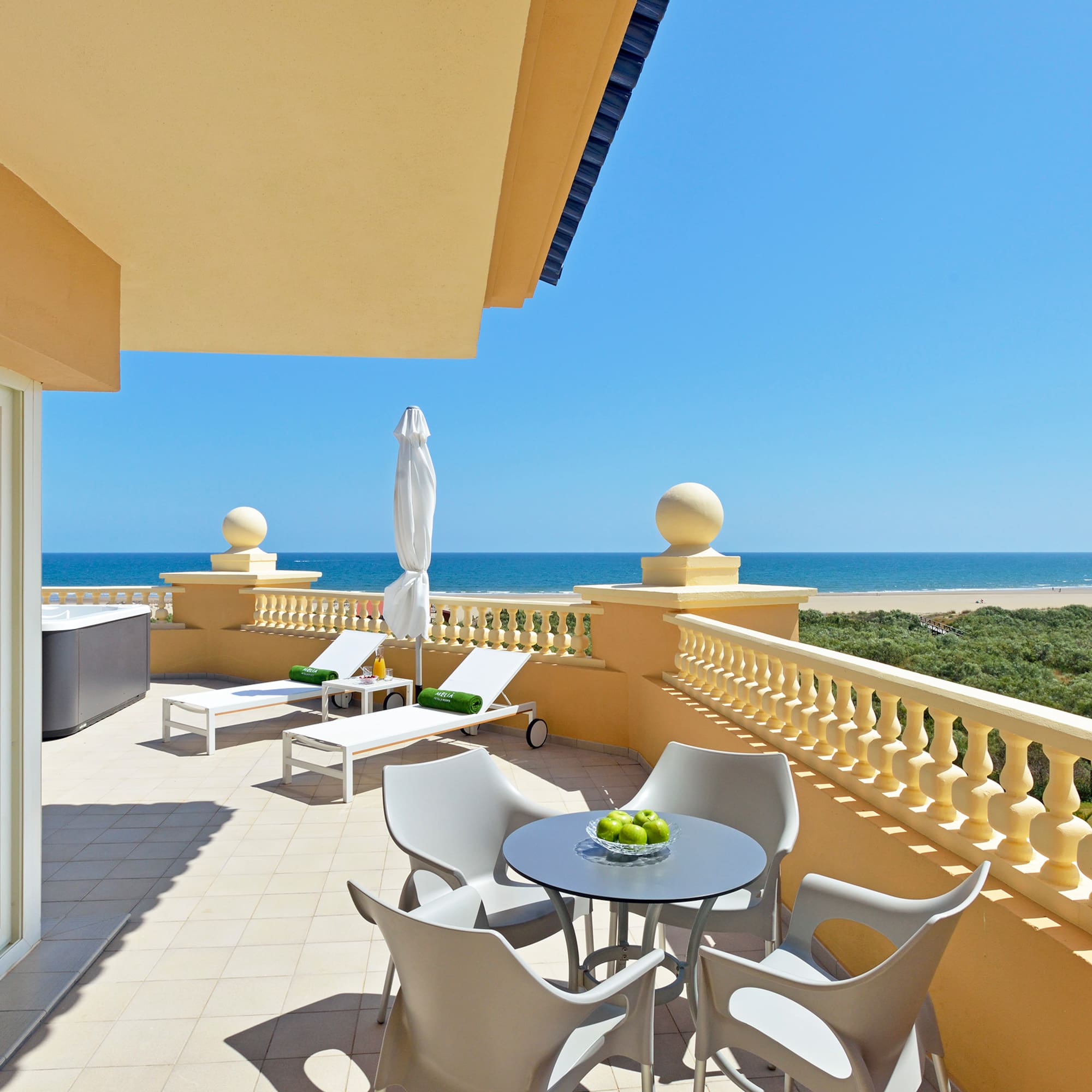 a patio with chairs and a table on a balcony overlooking the ocean