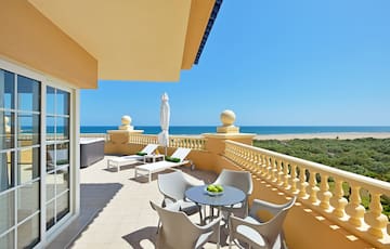 a patio with chairs and a table on a balcony overlooking the ocean