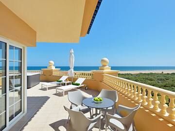 a patio with chairs and a table on a balcony overlooking the ocean