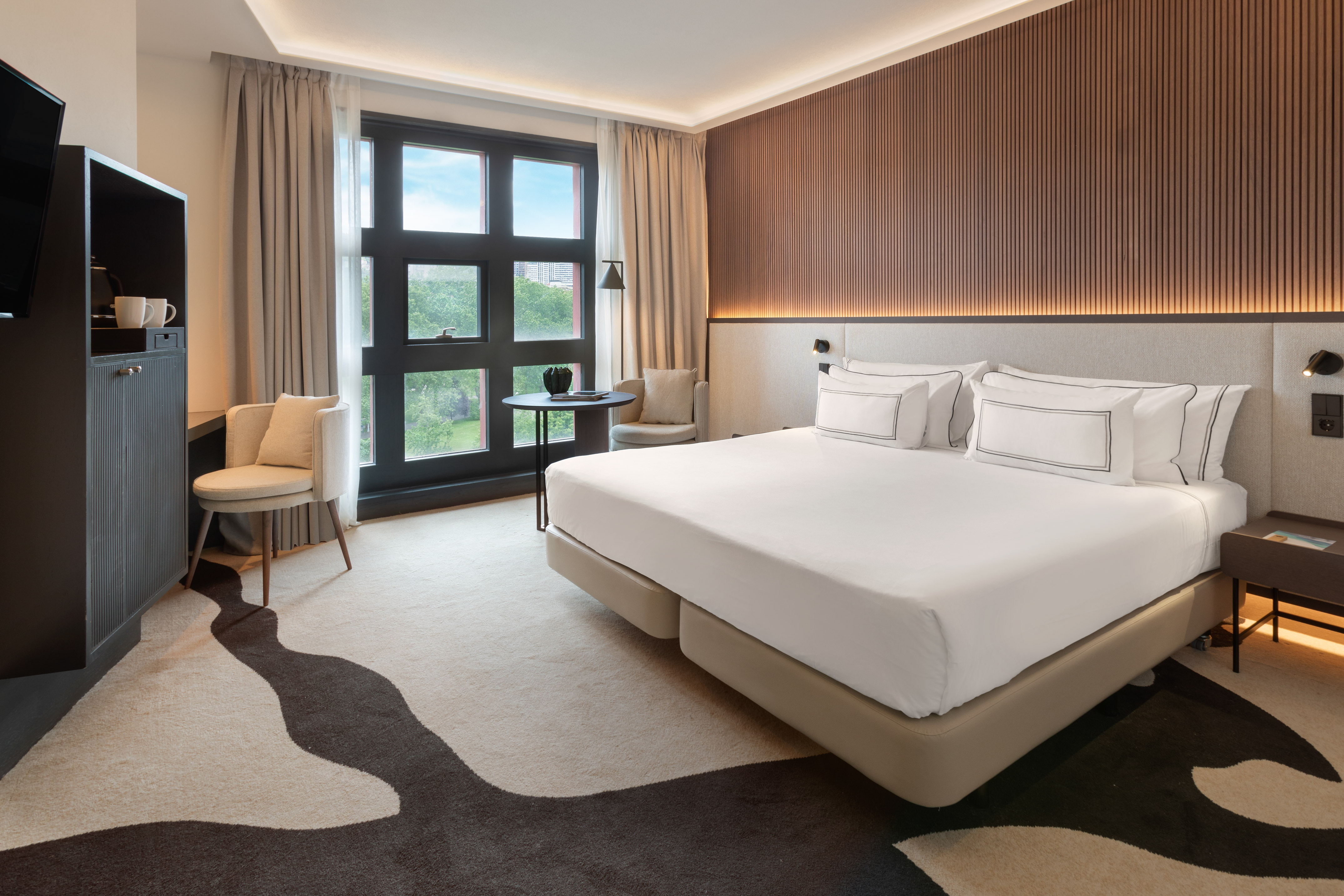 Modern hotel room with comfortable bed, large window, and stylish wooden wall.