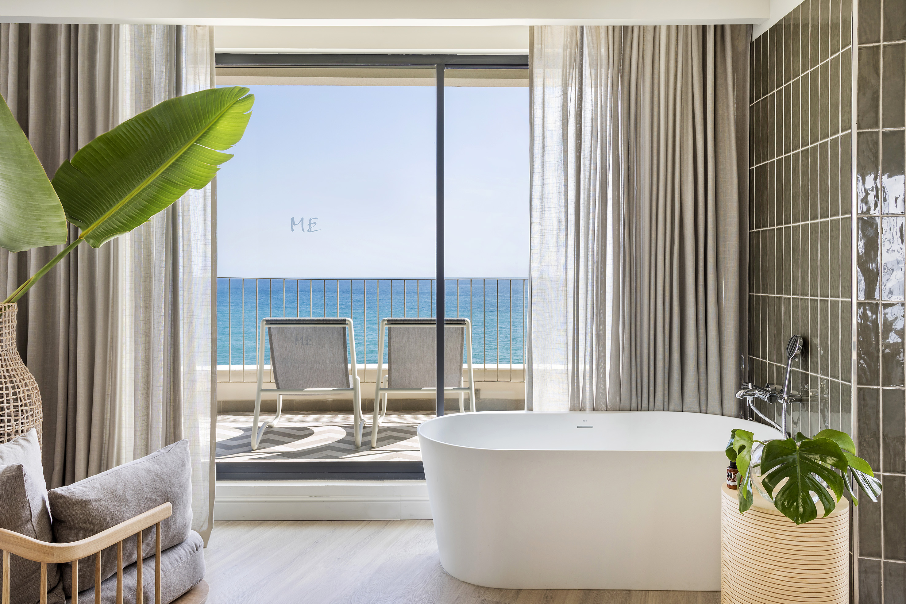 Luxury hotel bathroom with sea view, freestanding tub & balcony.