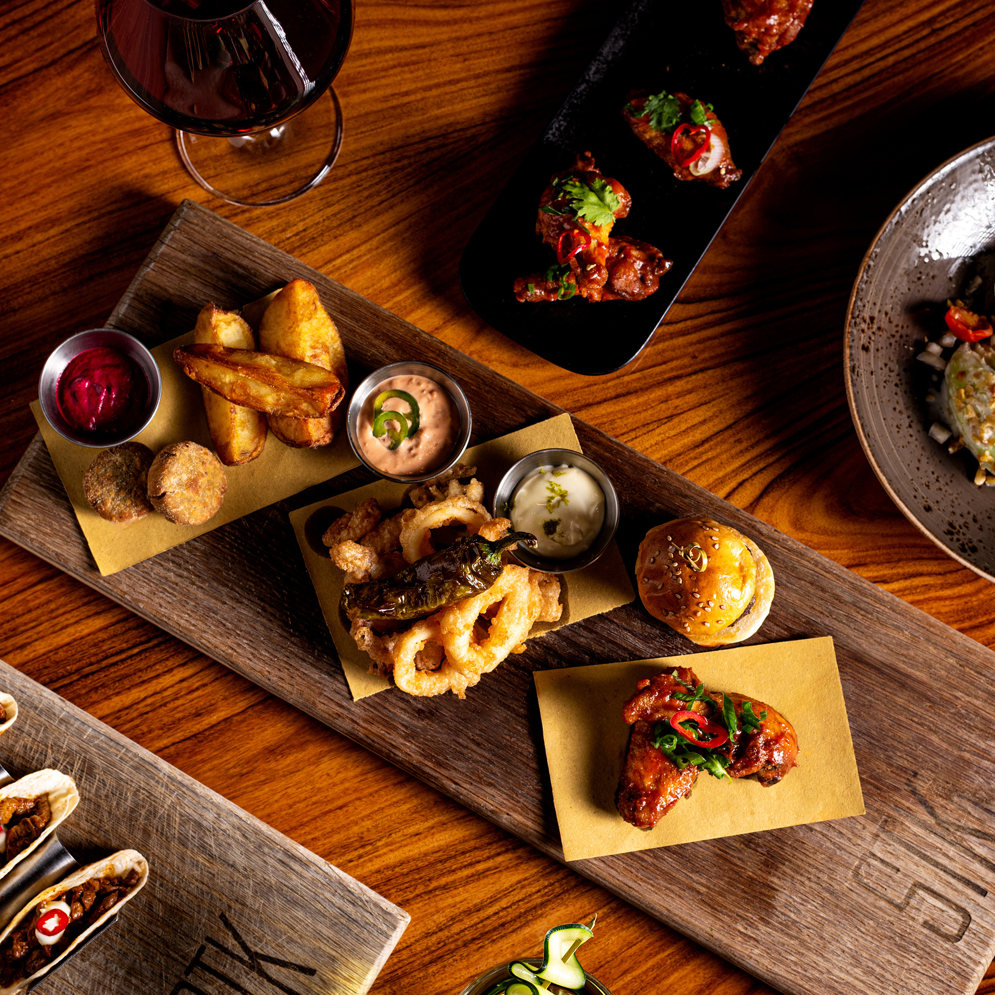 Restaurant appetizers: chicken wings, crispy calamari, fries, tacos, and red wine.