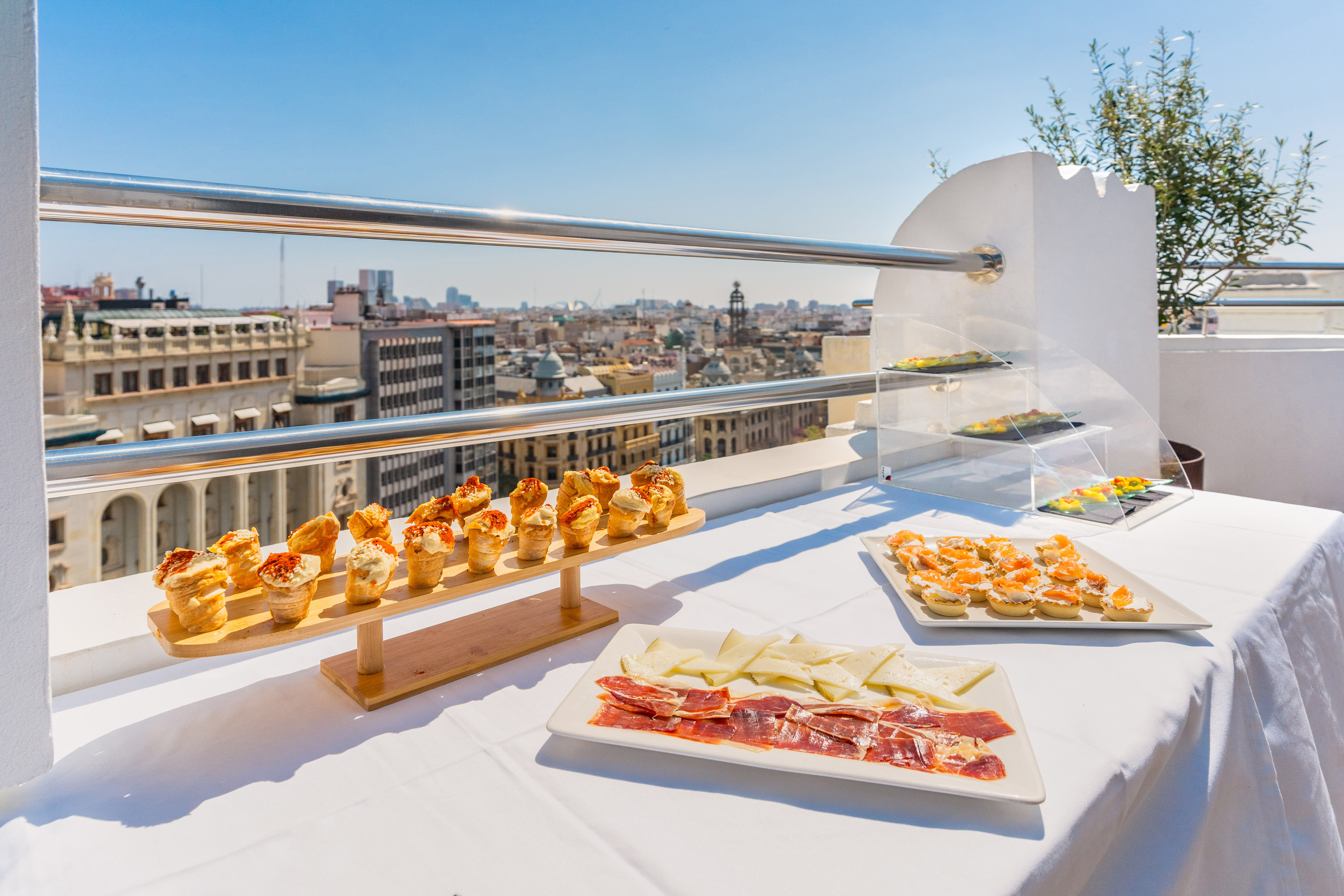 Rooftop catering: appetizers, ham, cheese, with a sunny city view.
