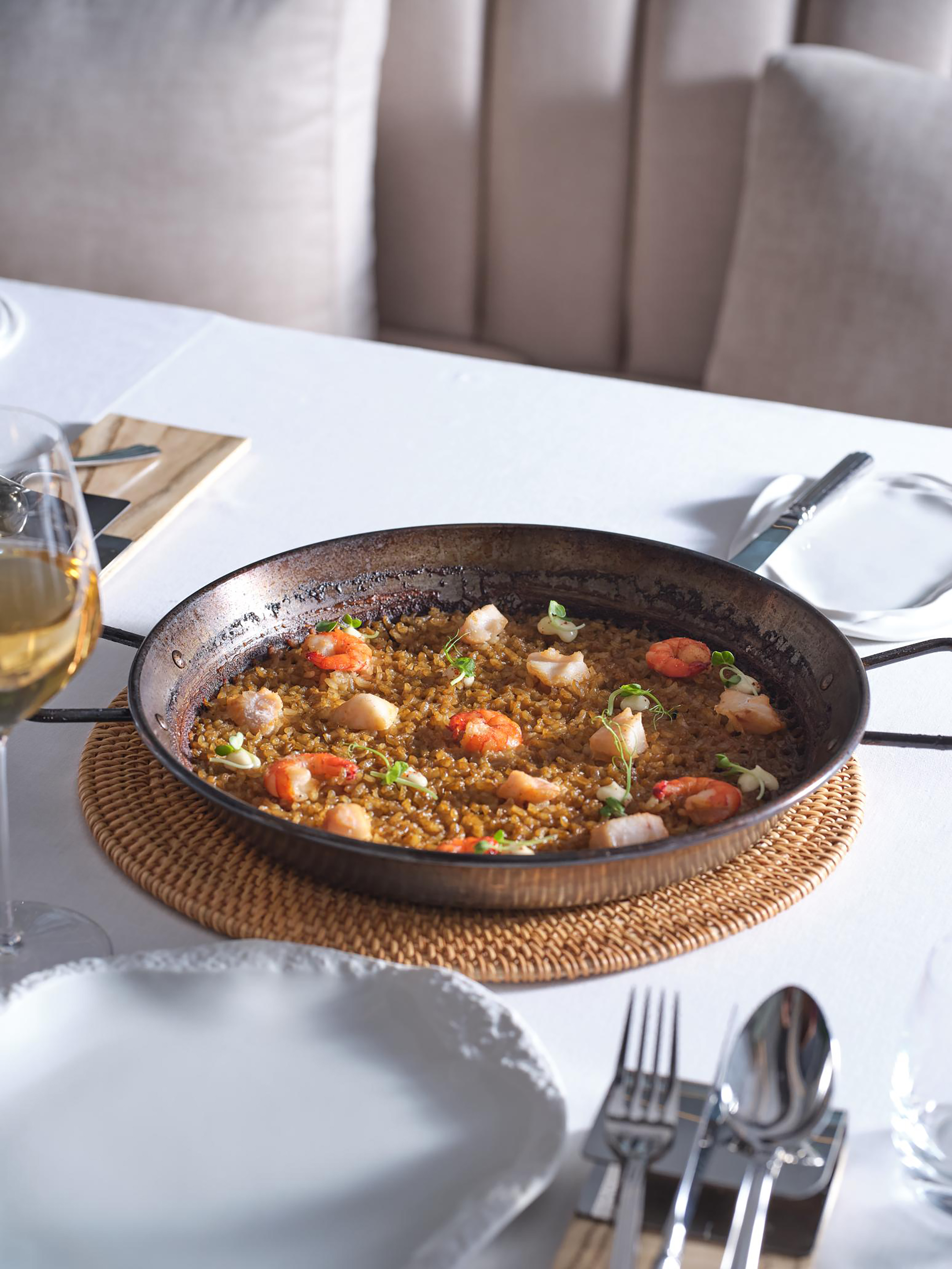 Seafood paella with shrimp and fish in a rustic pan on a restaurant table.
