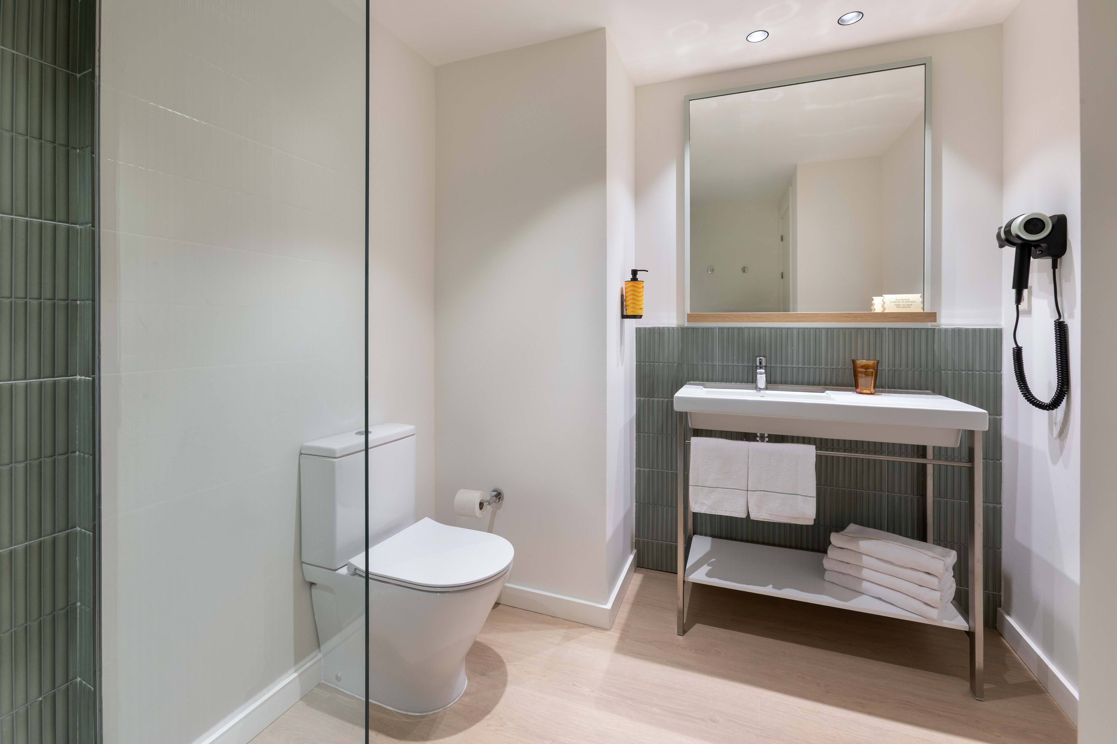 Modern bathroom with white toilet, vanity, mirror, and green accent wall tiles.