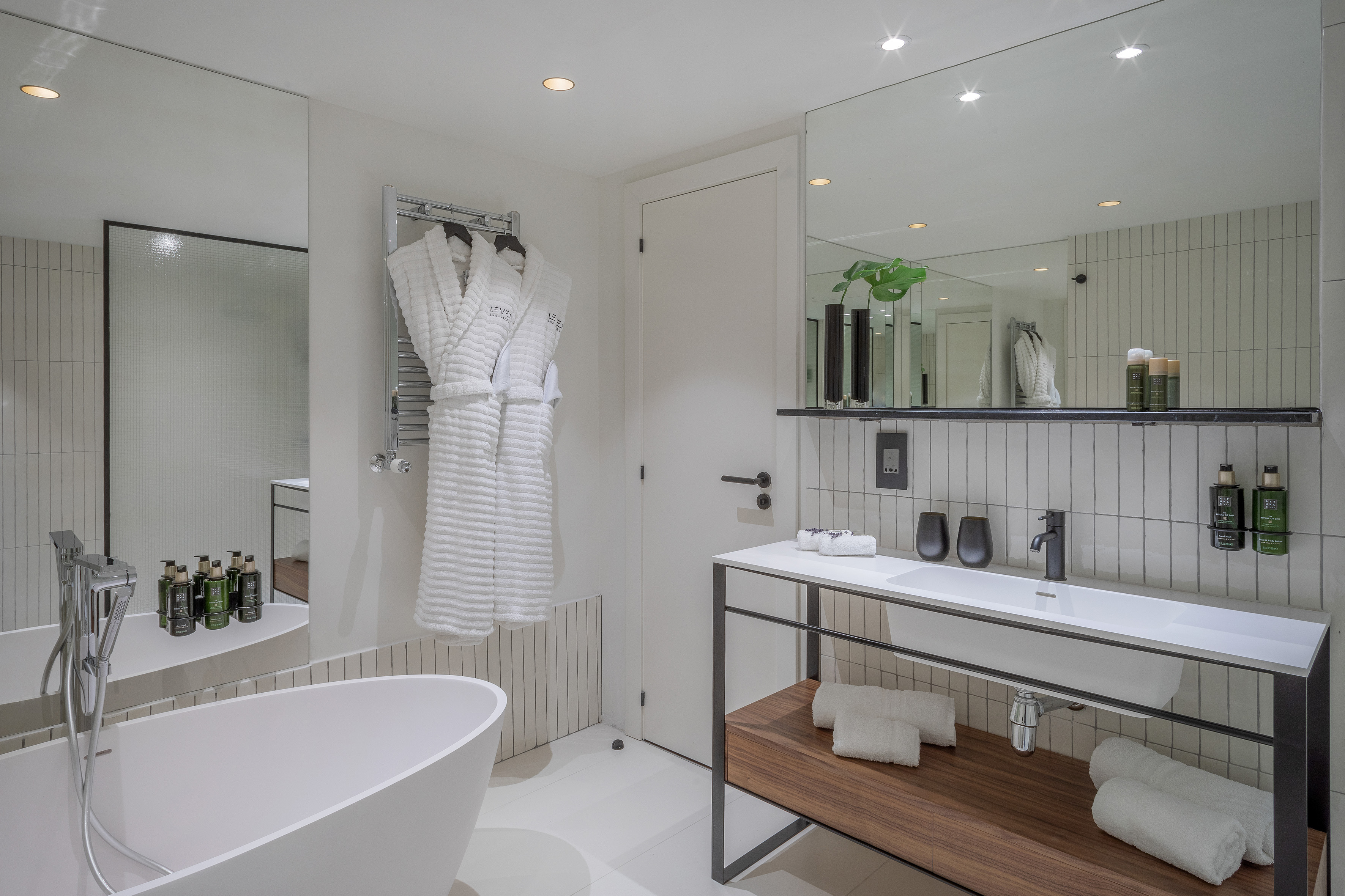 Clean modern bathroom with white tub, double robes, vanity, and large mirror.