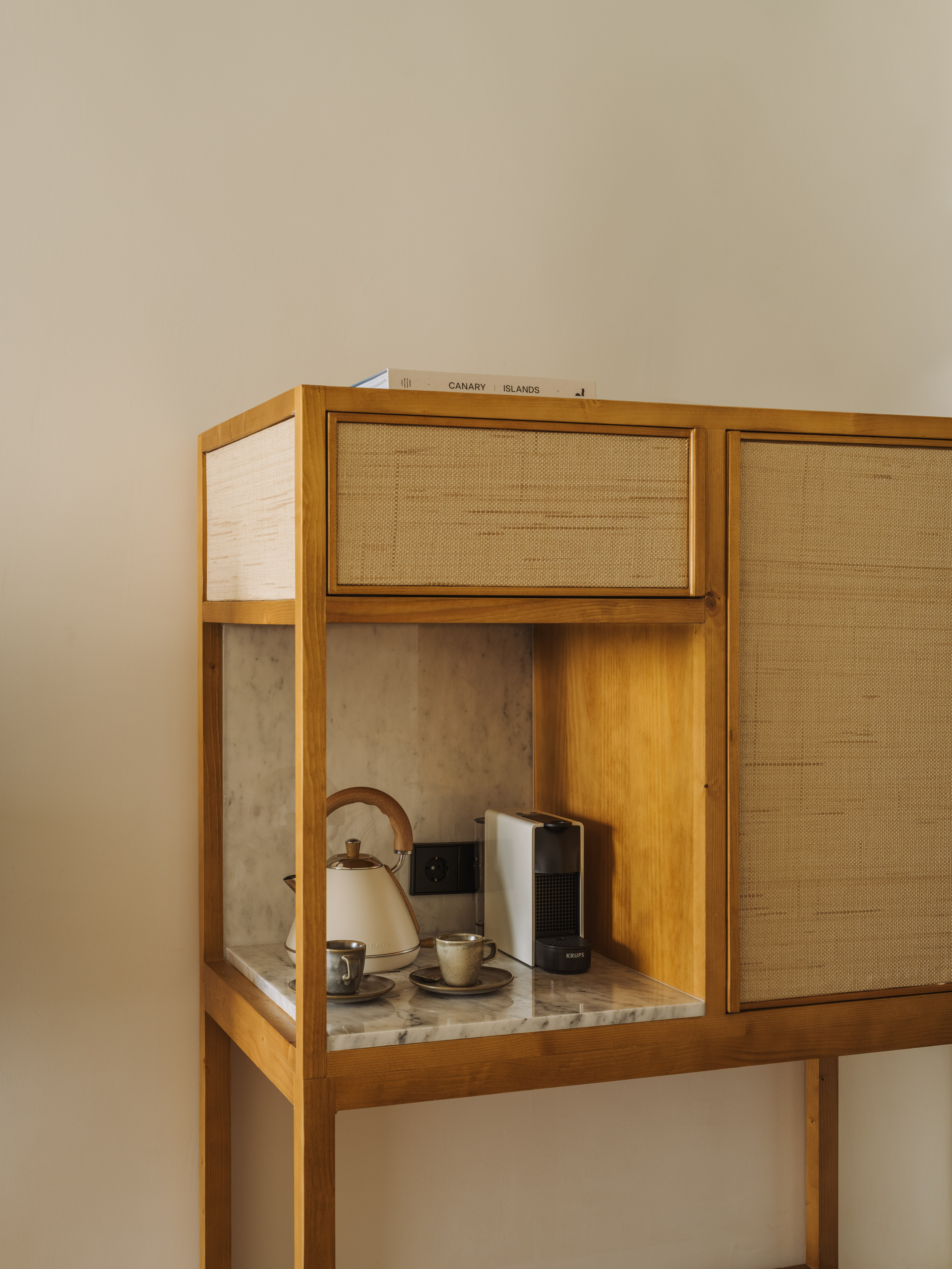 Wooden cabinet coffee station with kettle, Krups machine, cups on marble.